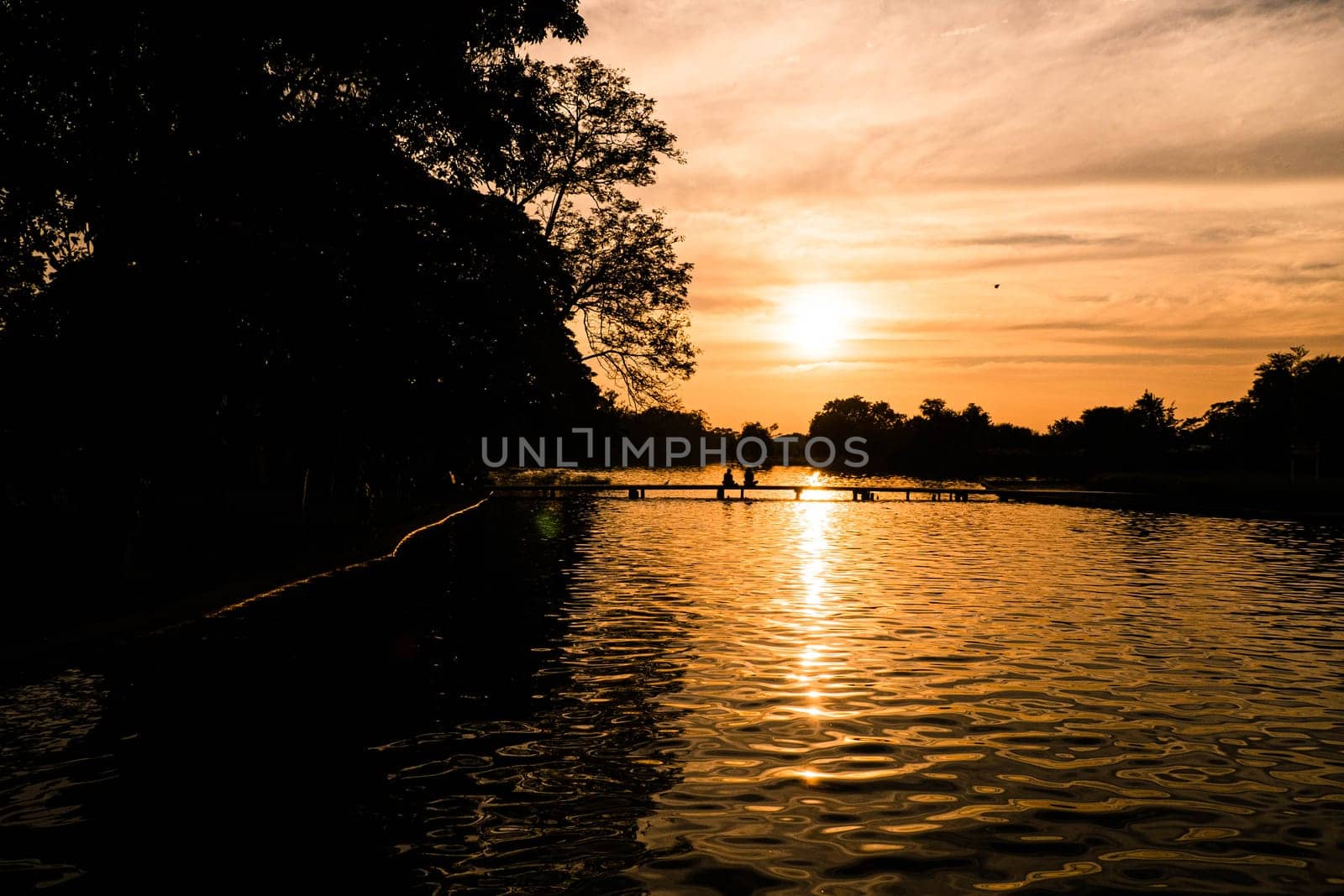 Lake landscape at sunset with Couple in love back light silhouette at lake orange sunset. Loving couple watching beautiful sunset