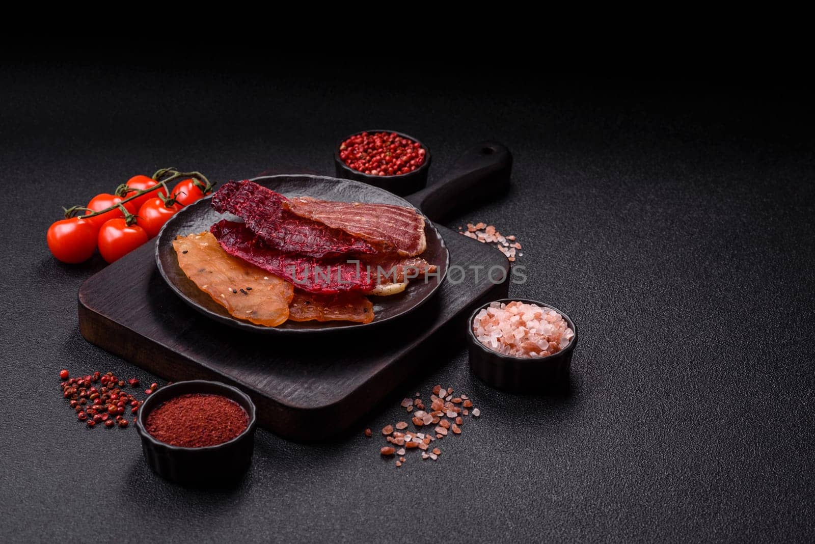 Jerky, dried meat in the form of slices with salt, spices and herbs on a dark concrete background