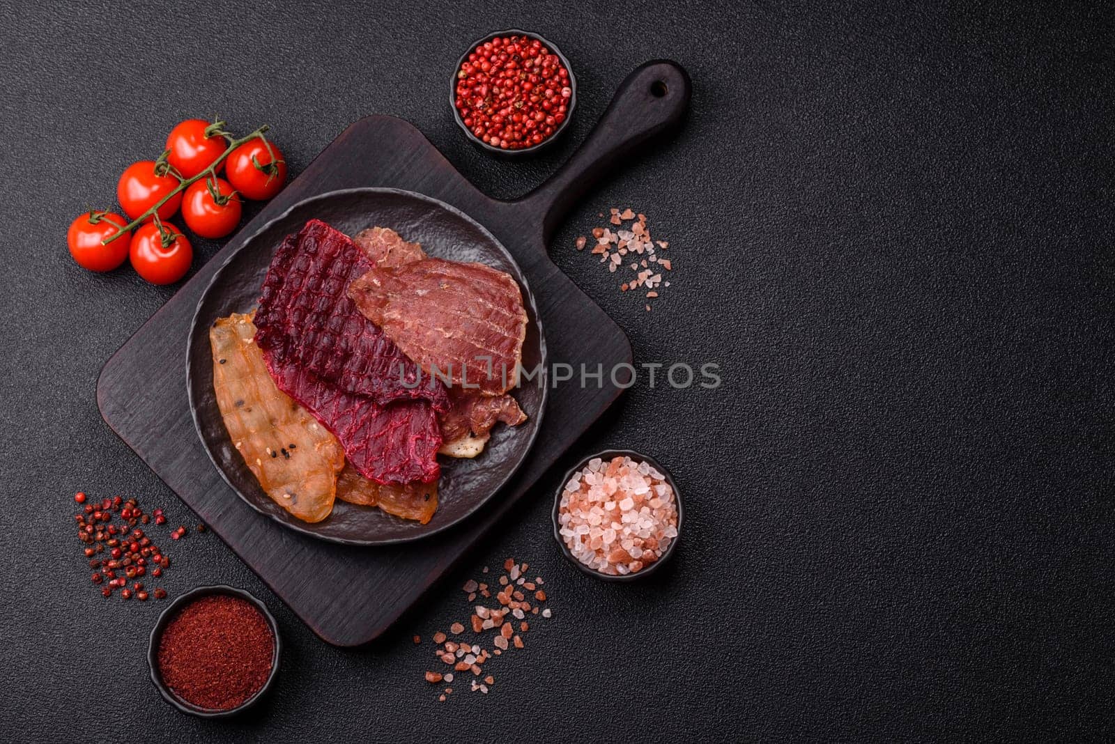 Jerky, dried meat in the form of slices with salt, spices and herbs on a dark concrete background