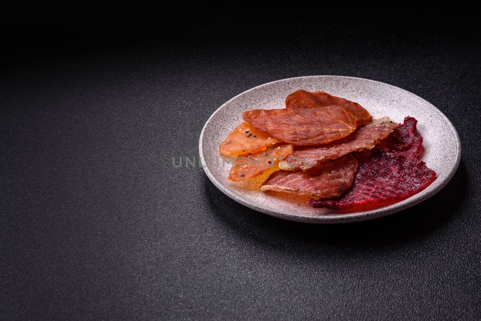 Jerky, dried meat in the form of slices with salt, spices and herbs on a dark concrete background