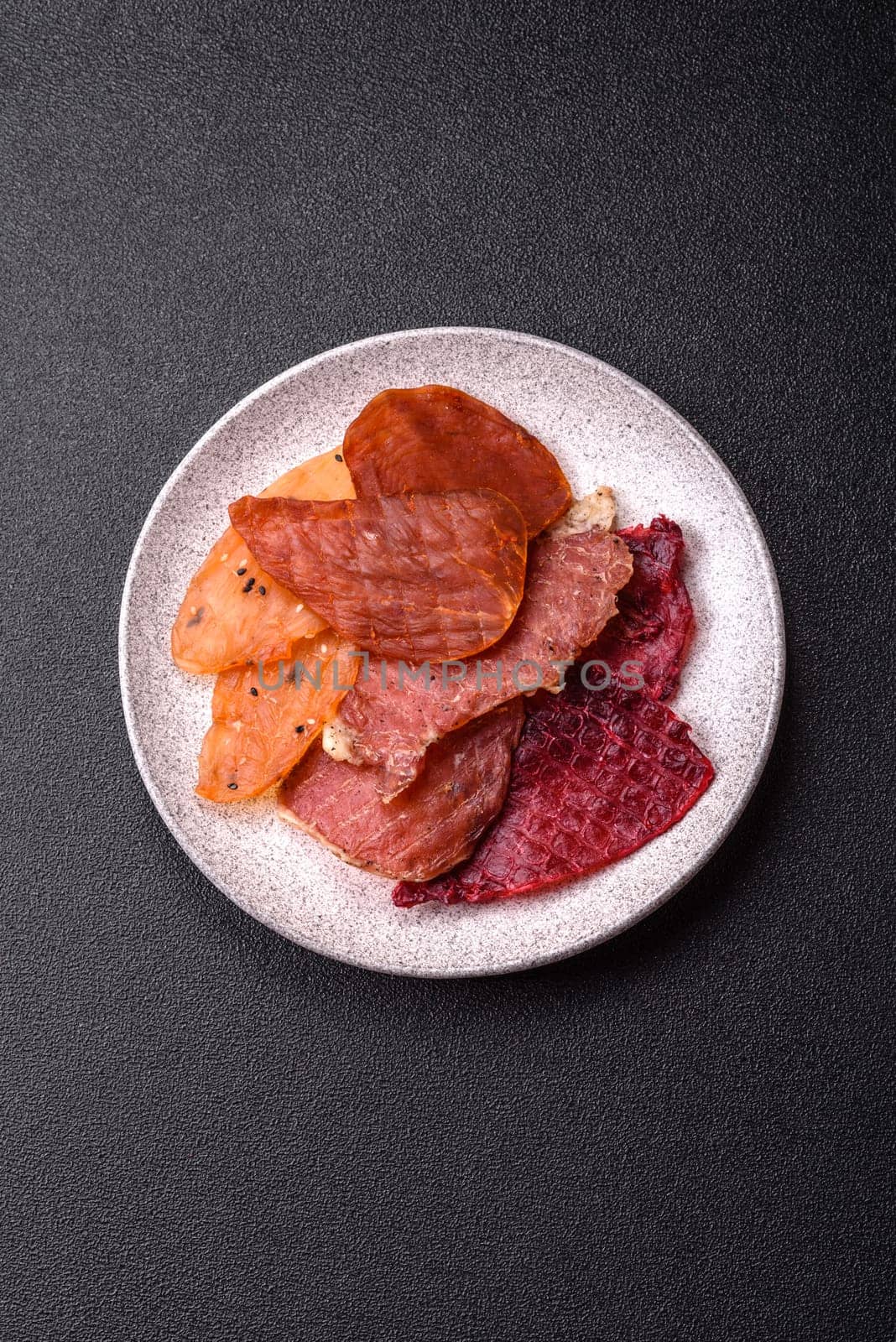 Jerky, dried meat in the form of slices with salt, spices and herbs on a dark concrete background
