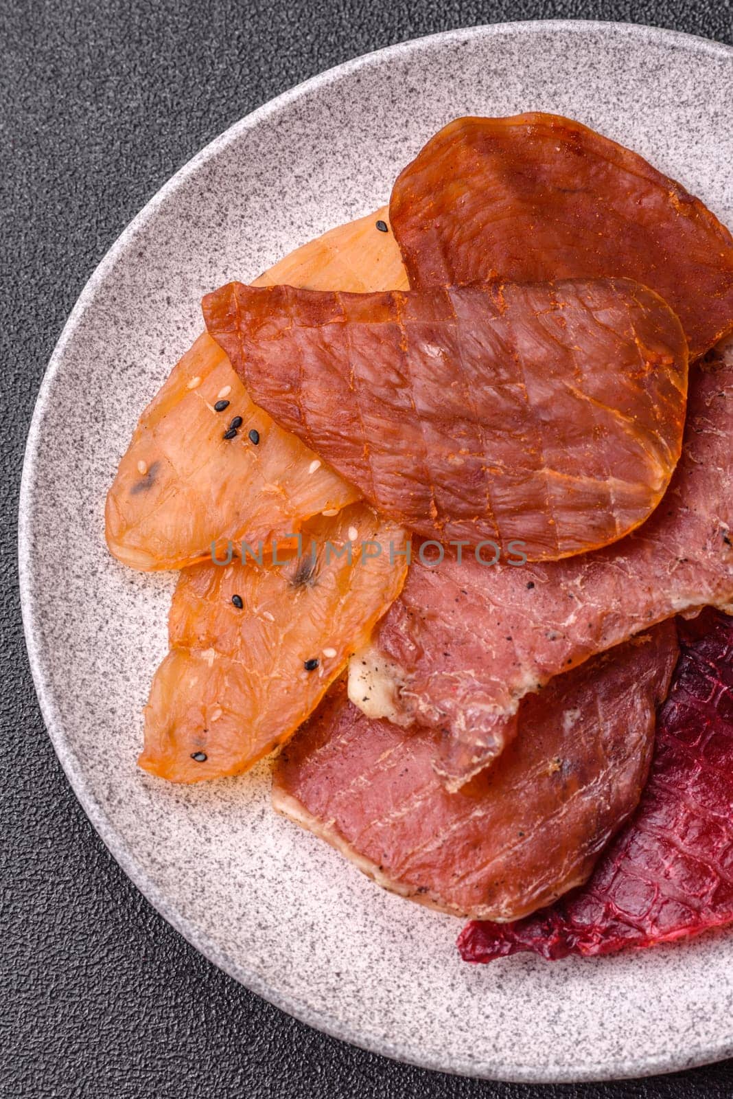 Jerky, dried meat in the form of slices with salt, spices and herbs on a dark concrete background
