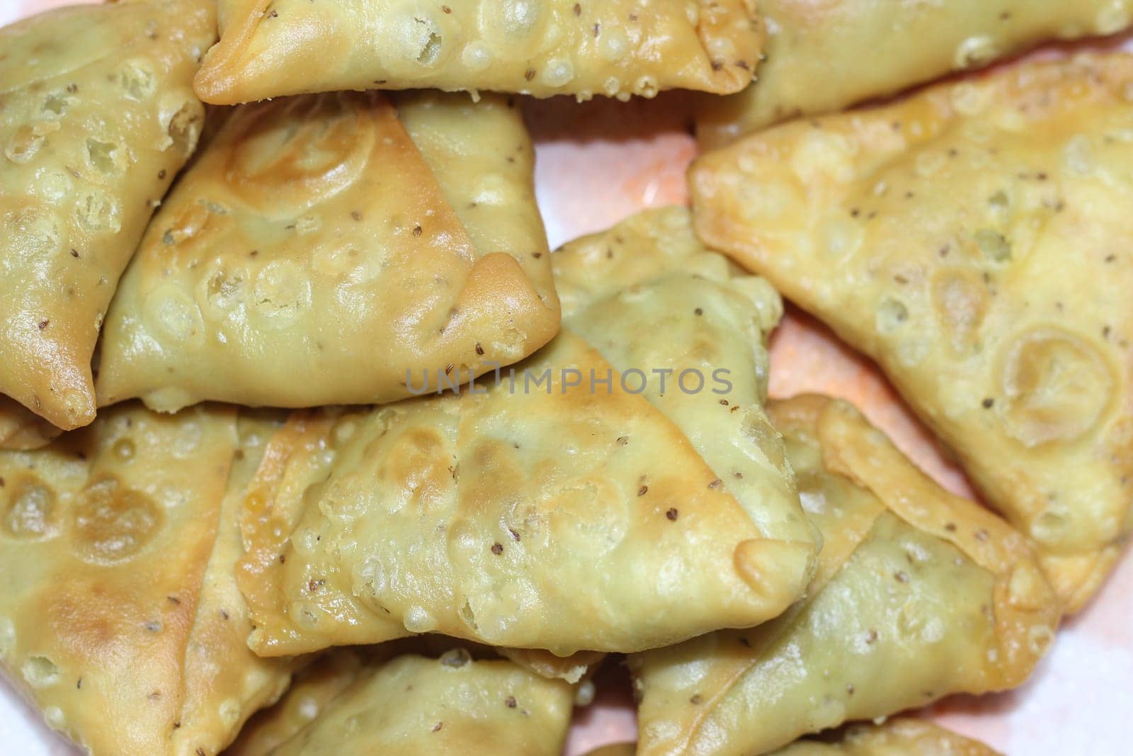 Closeup of delicious home made spicy and crunchy samosa pastries placed in a white ceramic plate on wooden floor