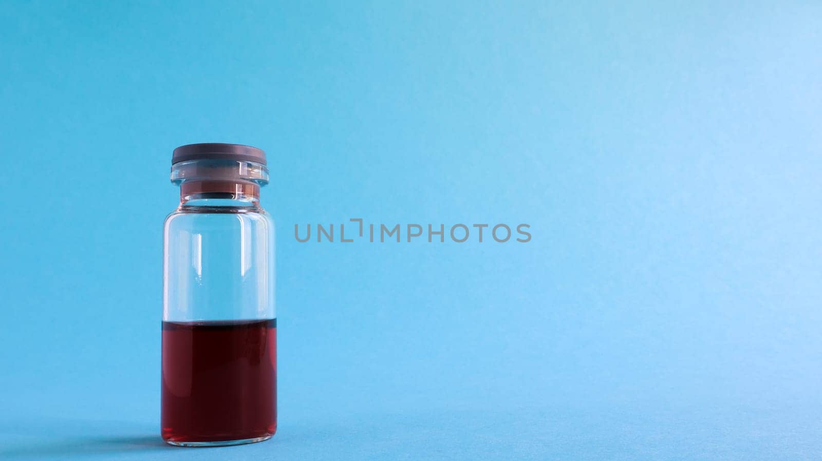 One glass transparent bottle with red medicine for vaccines on a blue background on a medical theme with copy space. Medical vaccination against the concept of coronavirus flu