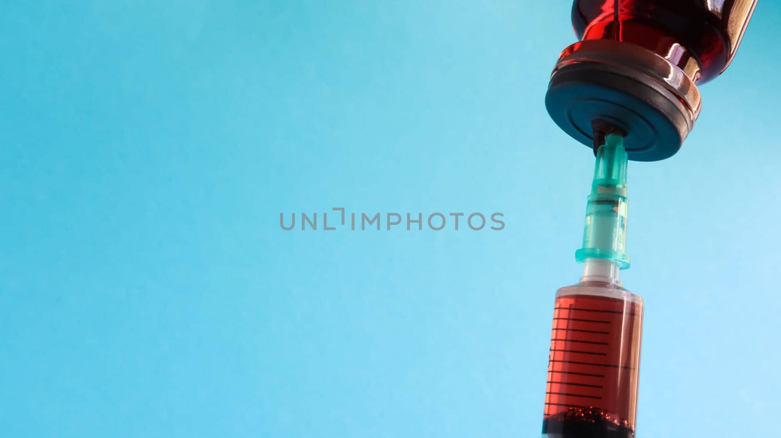 A syringe sticks out of a red liquid bottle. Isolated on a blue background. Medicine, injections, vaccines and disposable syringes, drug concept. Sterile bottle. Glass ampoule medical for injection