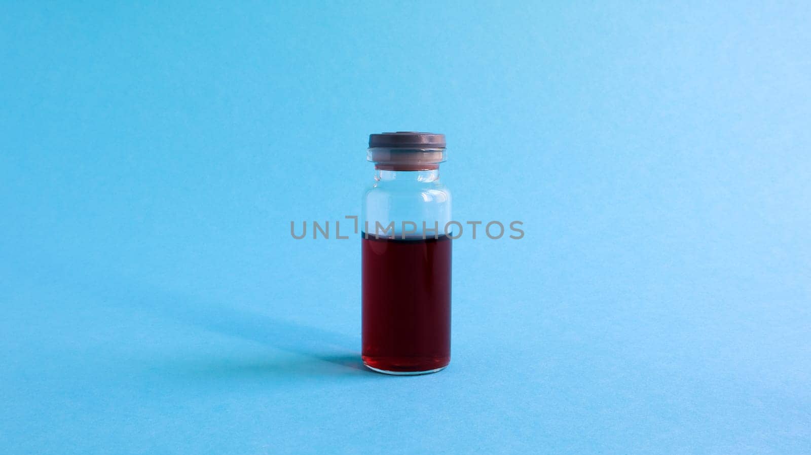 One glass transparent bottle with red medicine for vaccines on a blue background on a medical theme with copy space. Medical vaccination against the concept of coronavirus flu