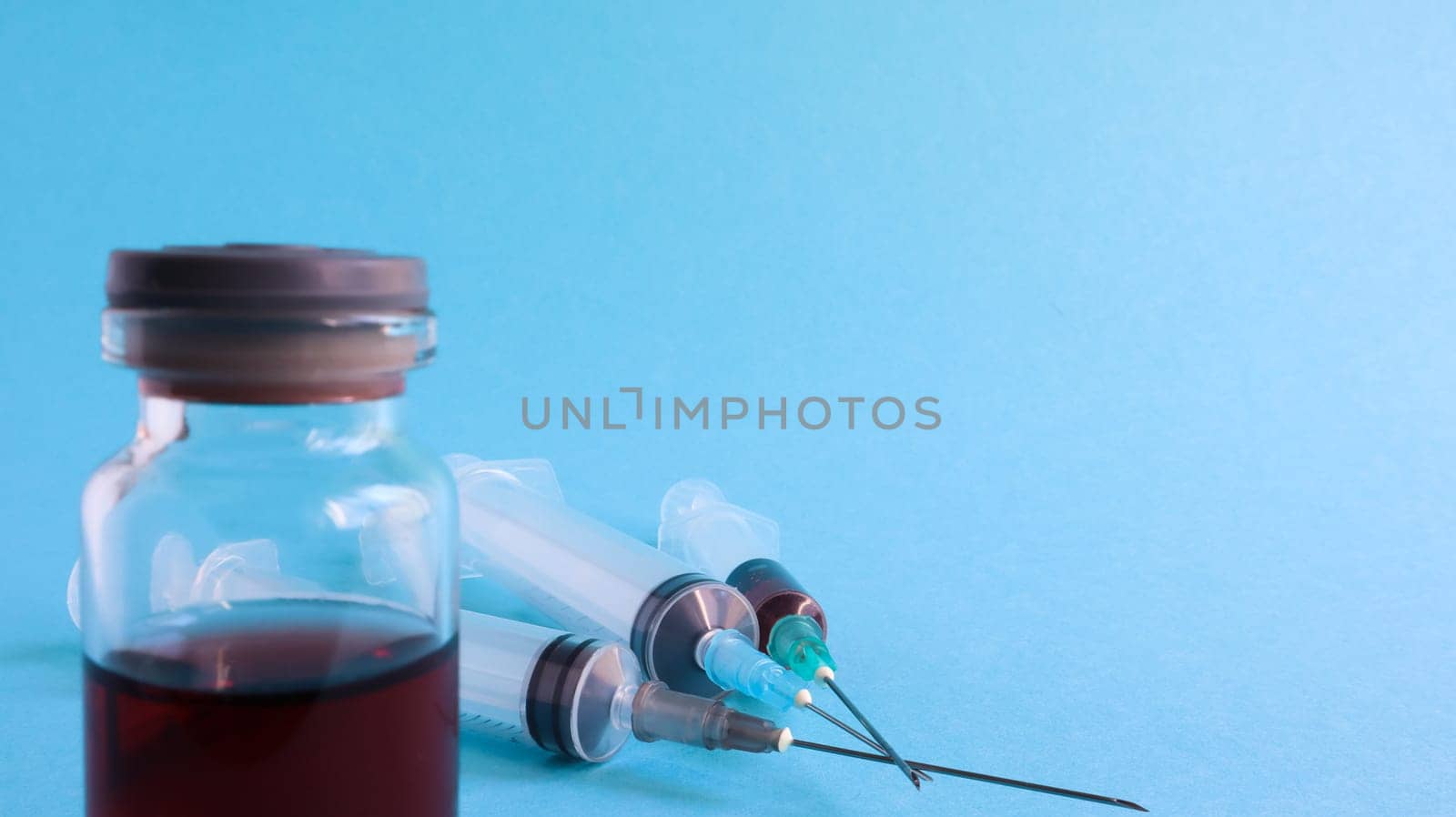 One medical glass bottle with red potion on a blue background and three medical disposable syringes. Medical concept shows a medical test tube and vaccines against coronavirus. Copy place.