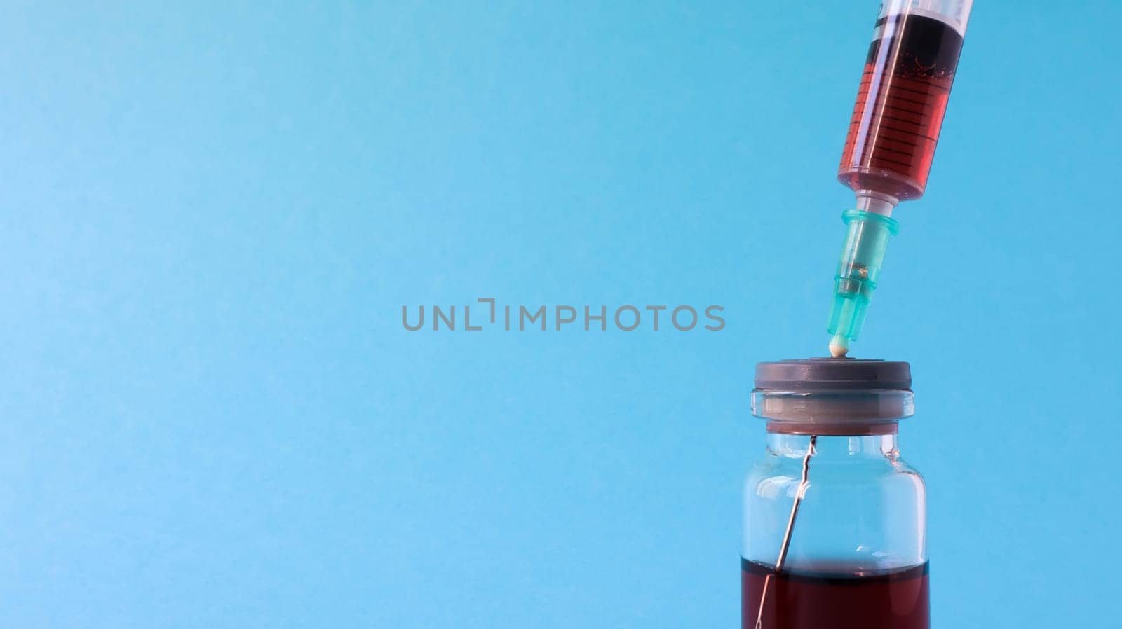 A syringe sticks out of a red liquid bottle. Isolated on a blue background. Medicine, injections, vaccines and disposable syringes, drug concept. Sterile bottle. Glass ampoule medical for injection