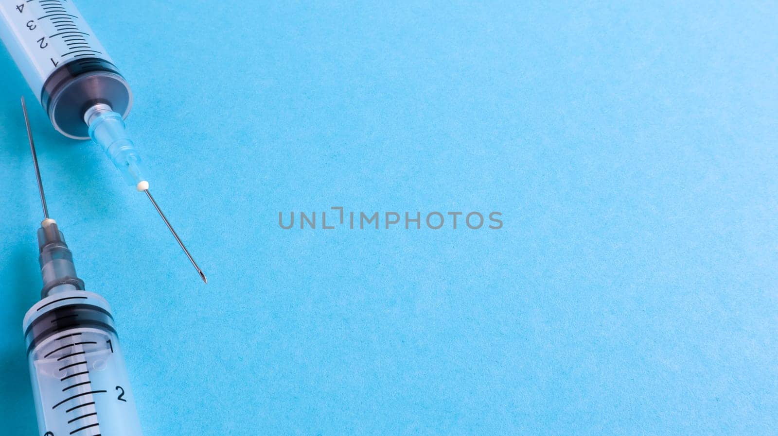 Two empty disposable plastic syringes with needles on a blue background not in the package. Vaccination concept. Medical tool for injection. copy space for text or logo.