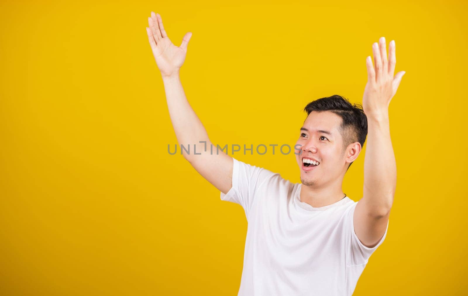 Asian handsome young man smile positive shaking hands enthusiastic shouting yes for win competition, male raising his fists Yes! with smiling delighted face, studio shot isolated on yellow background