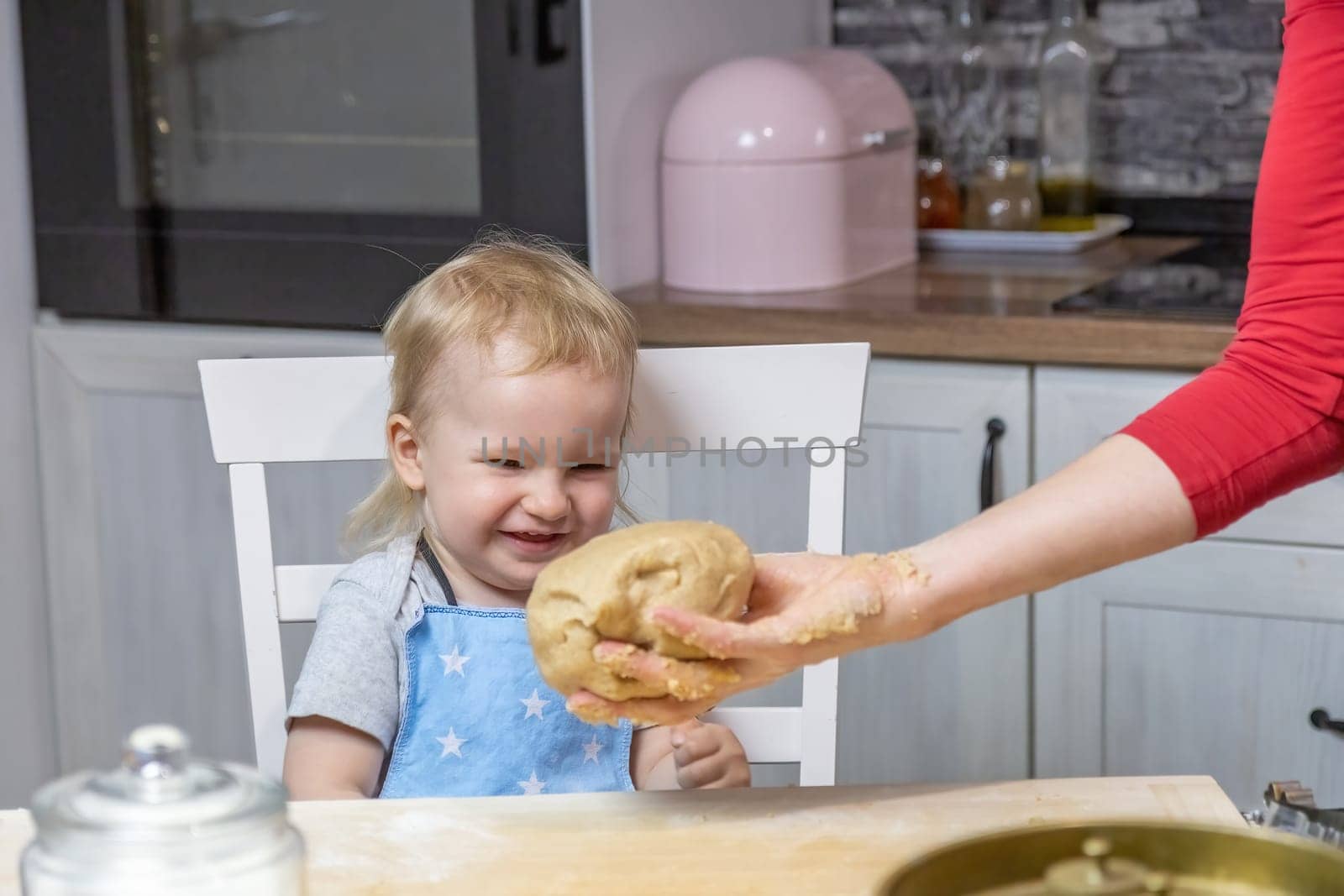 Adorable little child boy is laughing at the dough that a woman's hand is giving him. Horizontally.