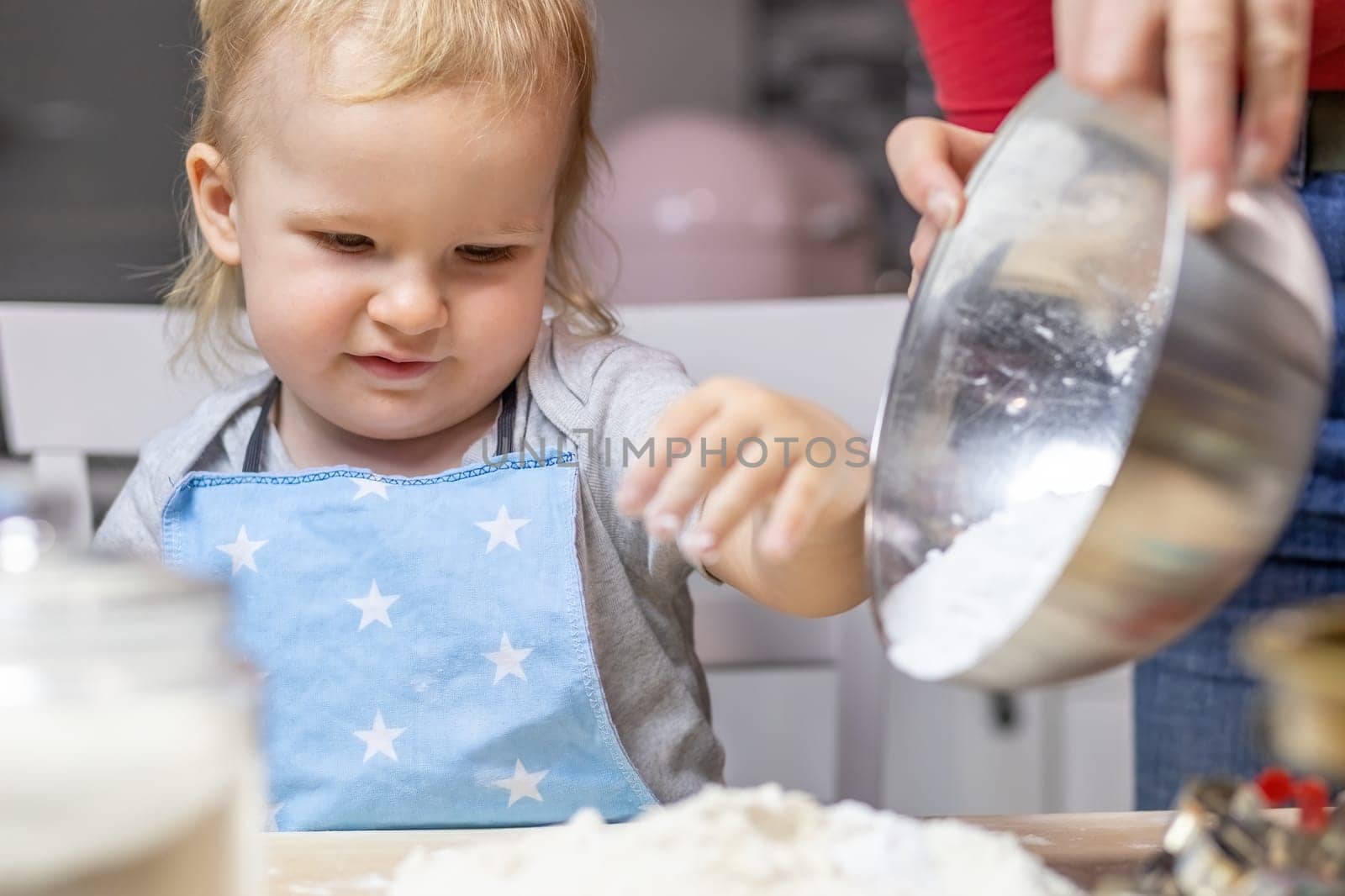 Blond little child boy is helpful in baking in domestic kitchen, indoors. Horizontally.
