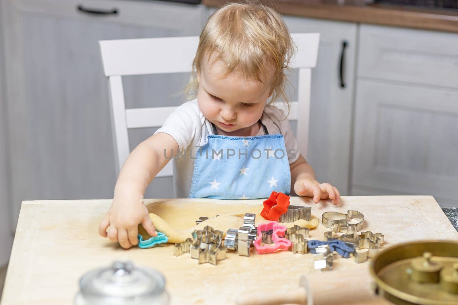 Adorable funny blond little child boy cuts out the dough in domestic kitchen. Horizontally.