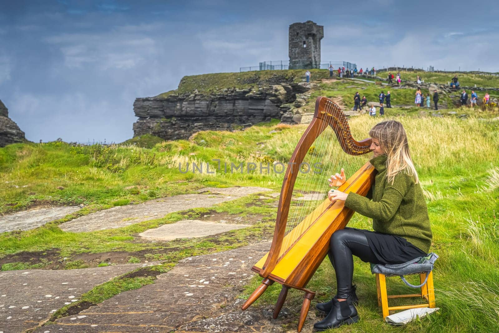 Doolin, Ireland, August 2019 Woman playing harp on the top of iconic Cliffs of Moher, popular tourist attraction, Wild Atlantic Way, County Clare