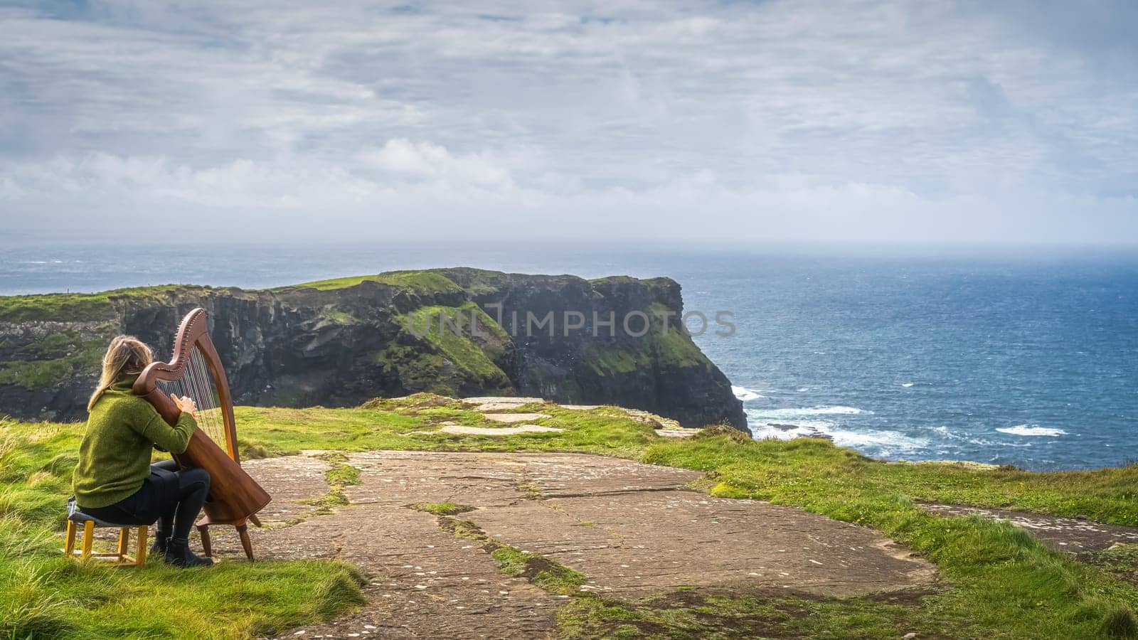 Woman playing harp on the top of iconic Cliffs of Moher, popular tourist attraction, Wild Atlantic Way, County Clare, Ireland