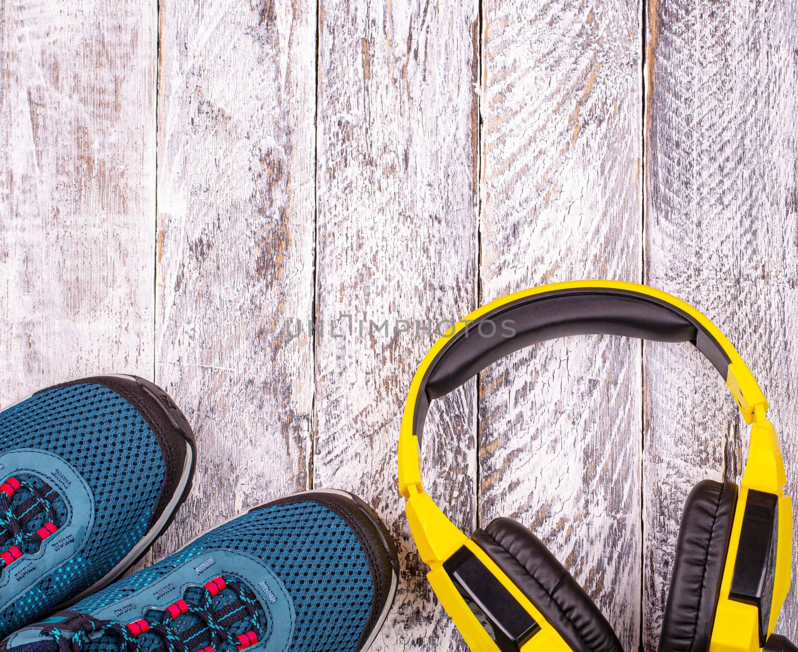 The Pair of blue women sneakers and yellow headphones on white wooden background
