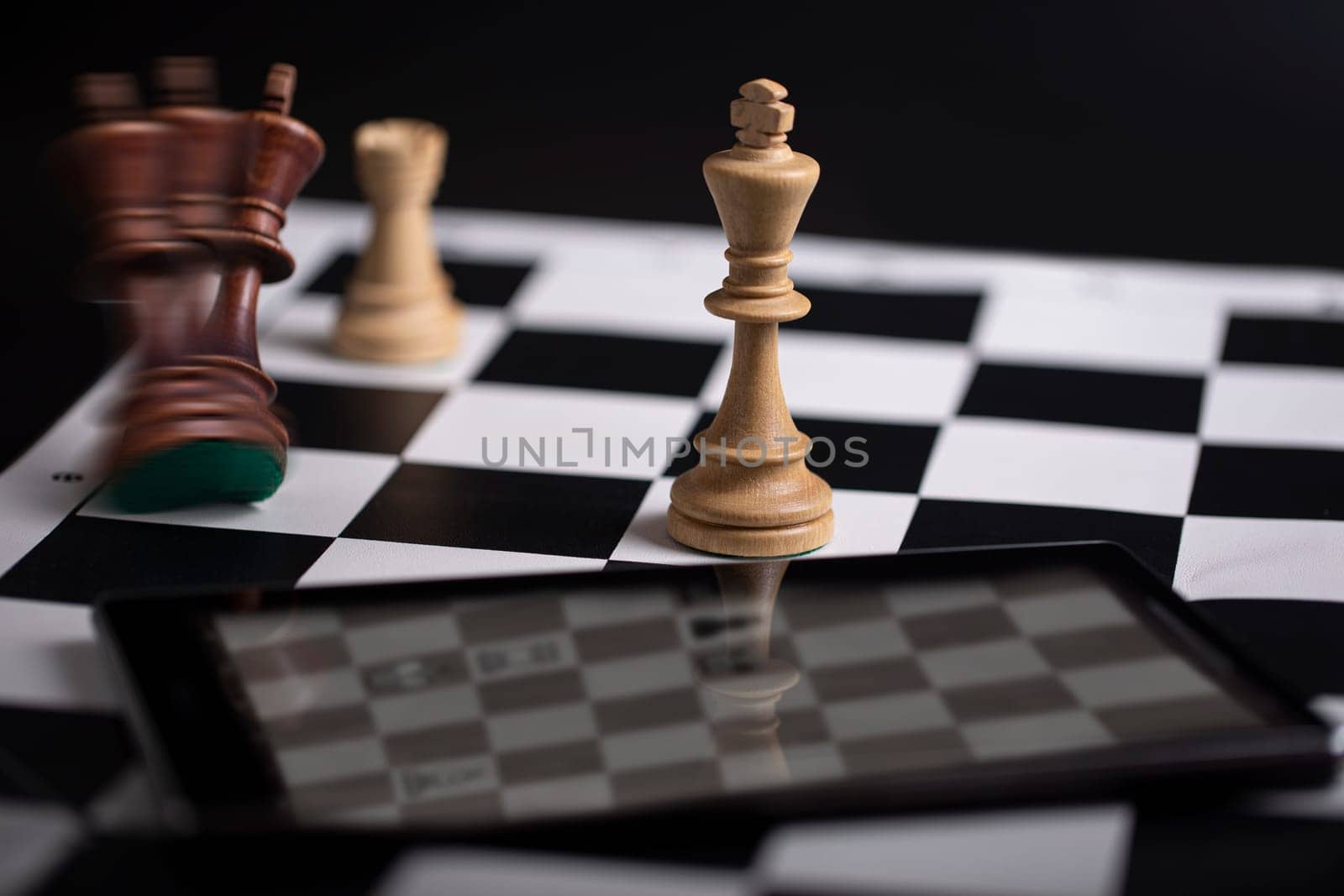 The Chess pieces on a chessboard and smartphone. The concept of playing and winning a chess tournament