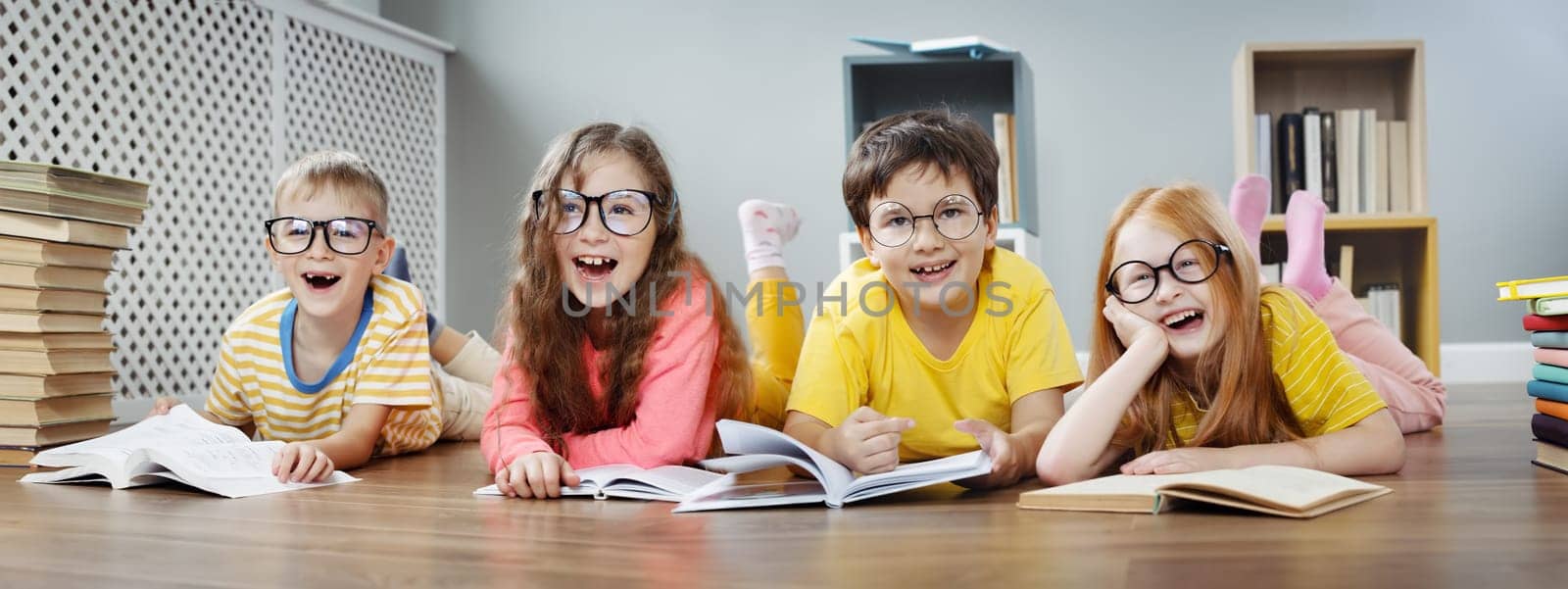 Four cute children in glasses lying on the floor indoors with books. Concept of hobby and education.