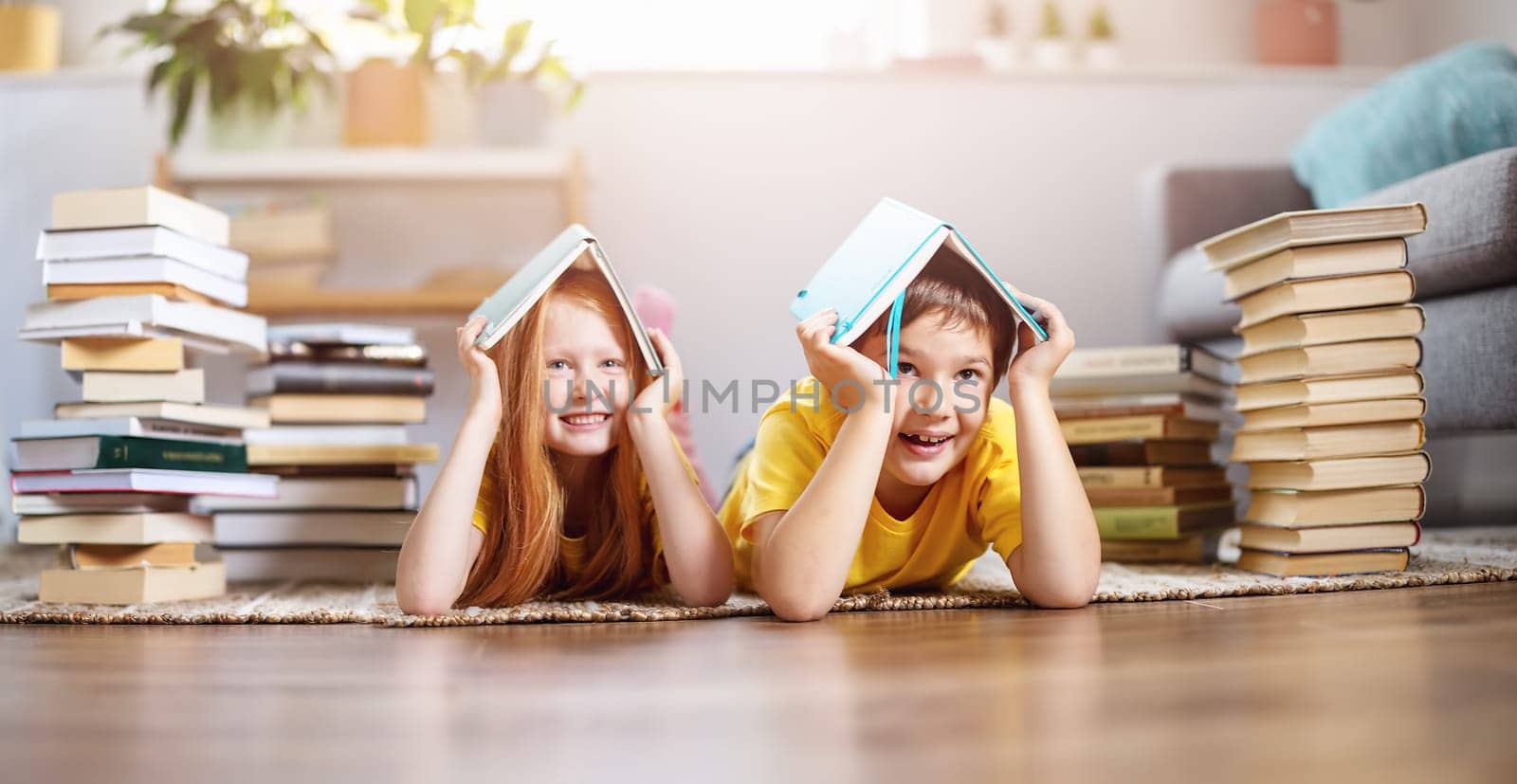 Two cute children lying on the floor indoors with books on the head. Concept of hobby and education.