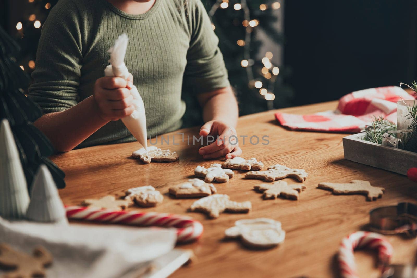 Merry Christmas, Happy New Year. A little small baby girl decorates cookies with protein white cream using culinary bag. Festive gingerbread cooking, baking. Family time, preparation for holidays