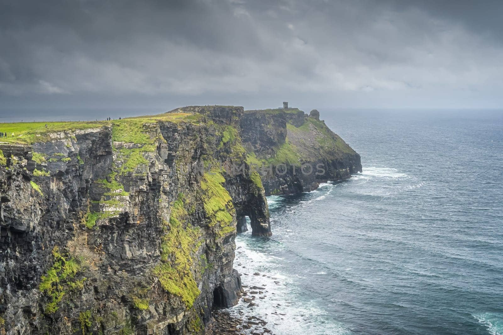 Tourists sightseeing Cliffs of Moher with watchtower Moher Tower on far distance, popular tourist attraction, Wild Atlantic Way, County Clare, Ireland