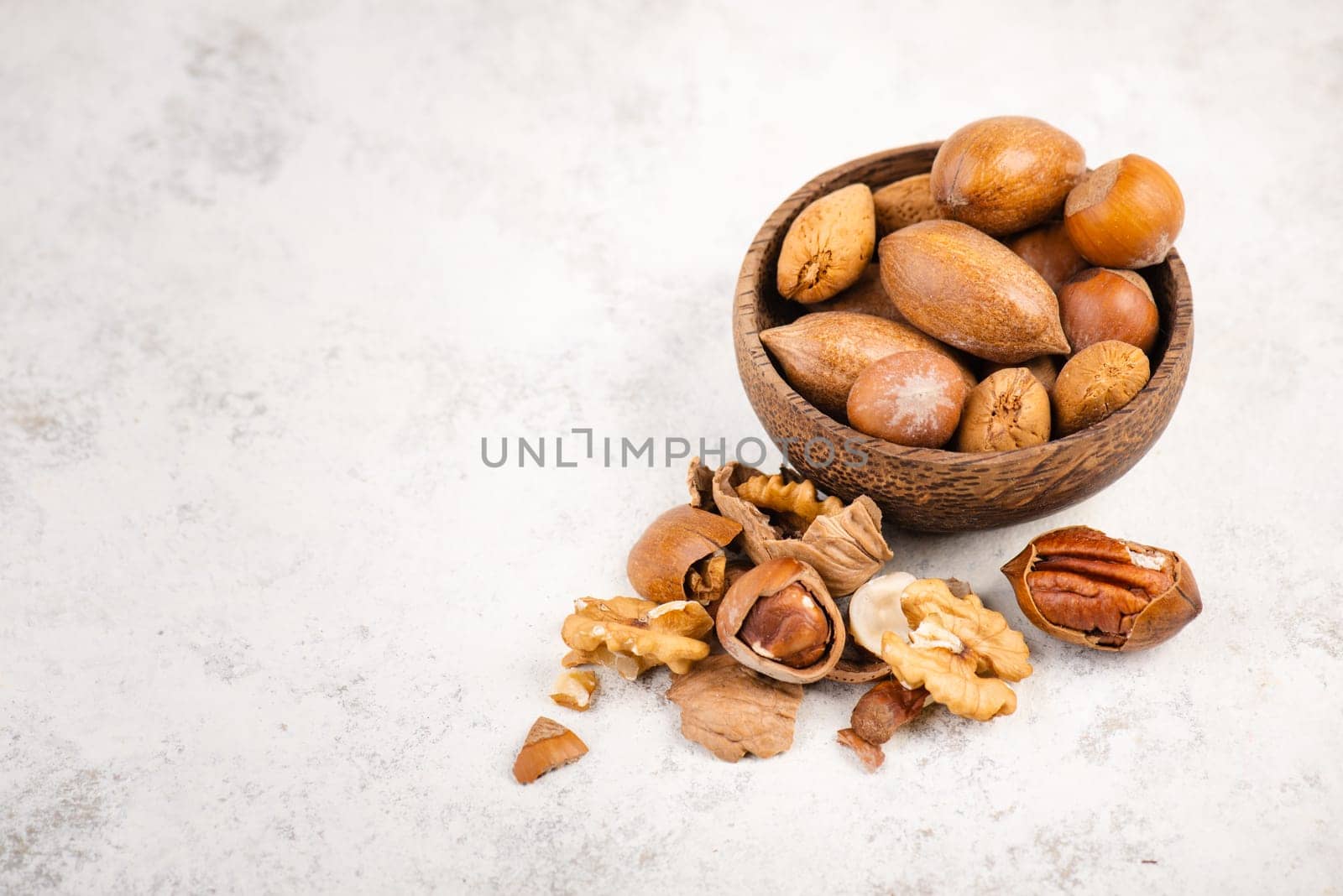Mix of nuts, like hazelnuts, walnuts in a wooden bowl on a textured background, empty copy space for text