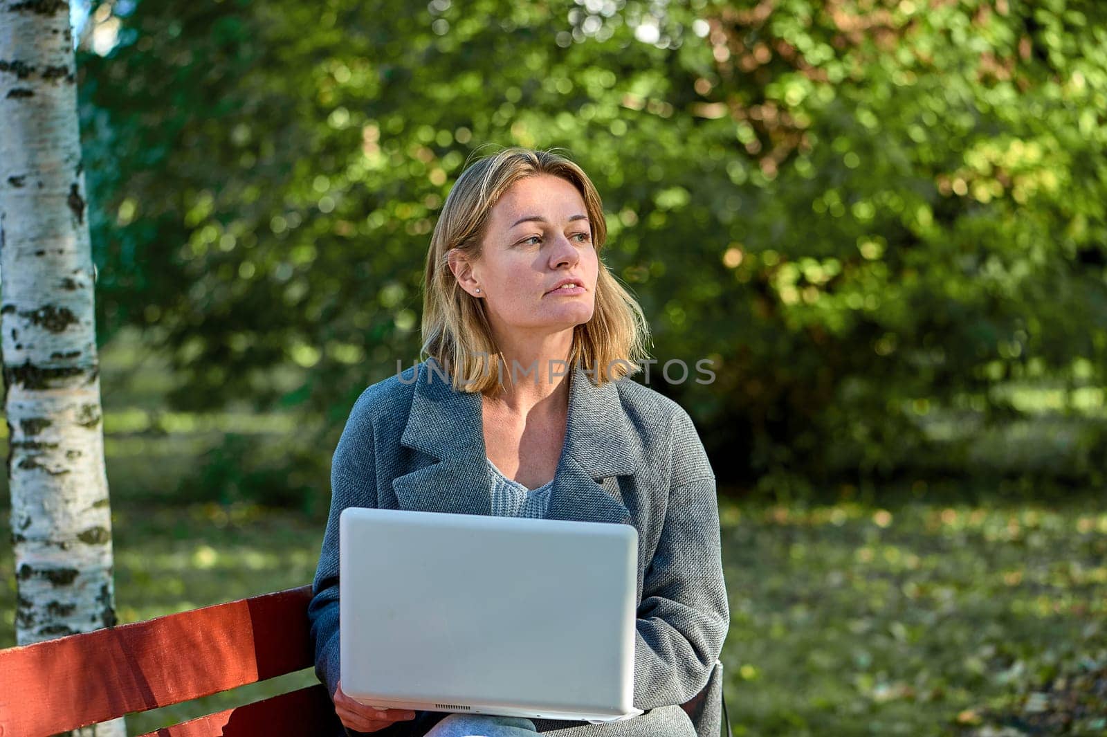 A woman with a laptop is sitting on a park bench on a sunny summer day. High quality photo