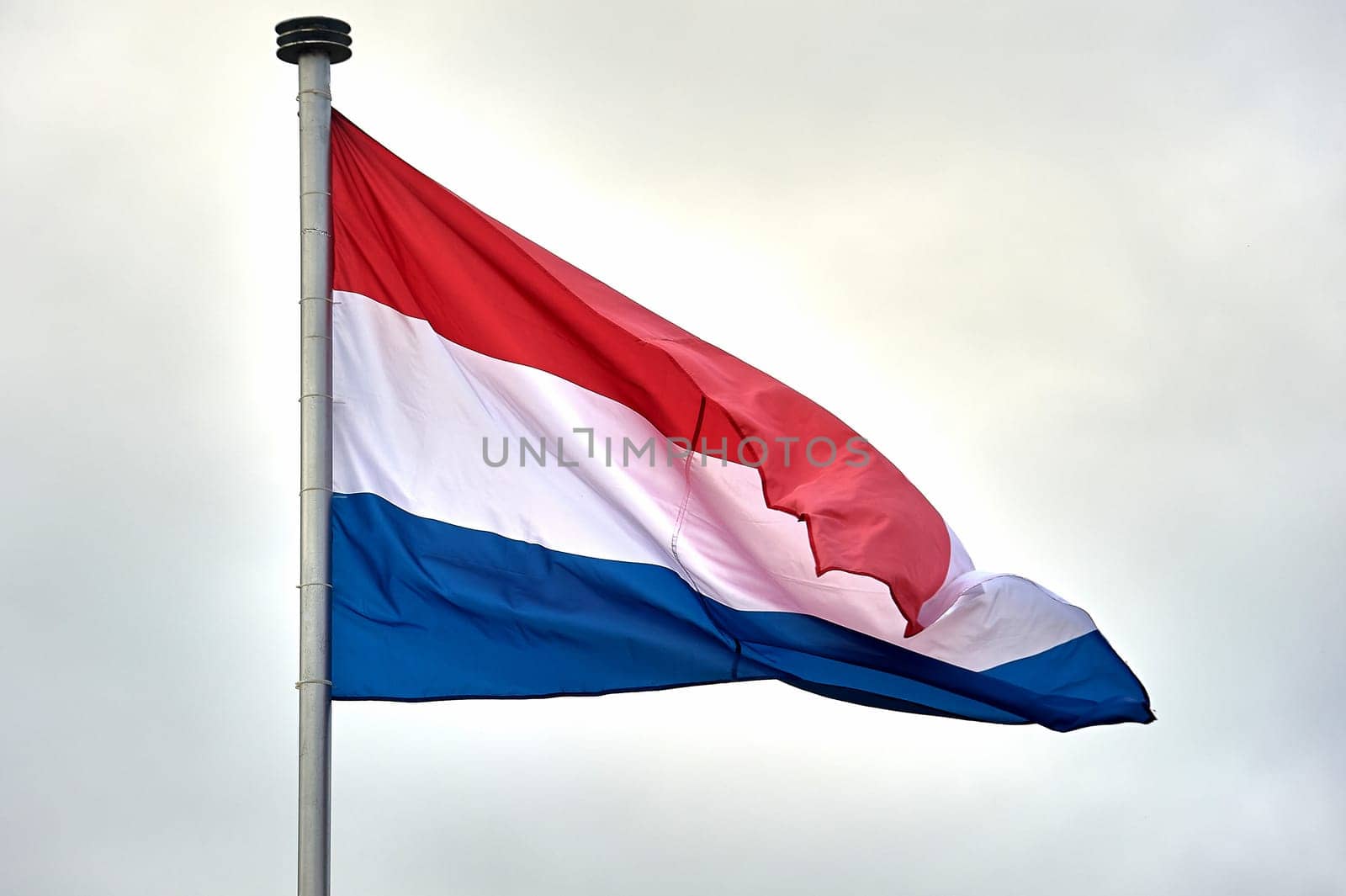 The flag of the Netherlands hangs on a metal flagpole. High quality photo