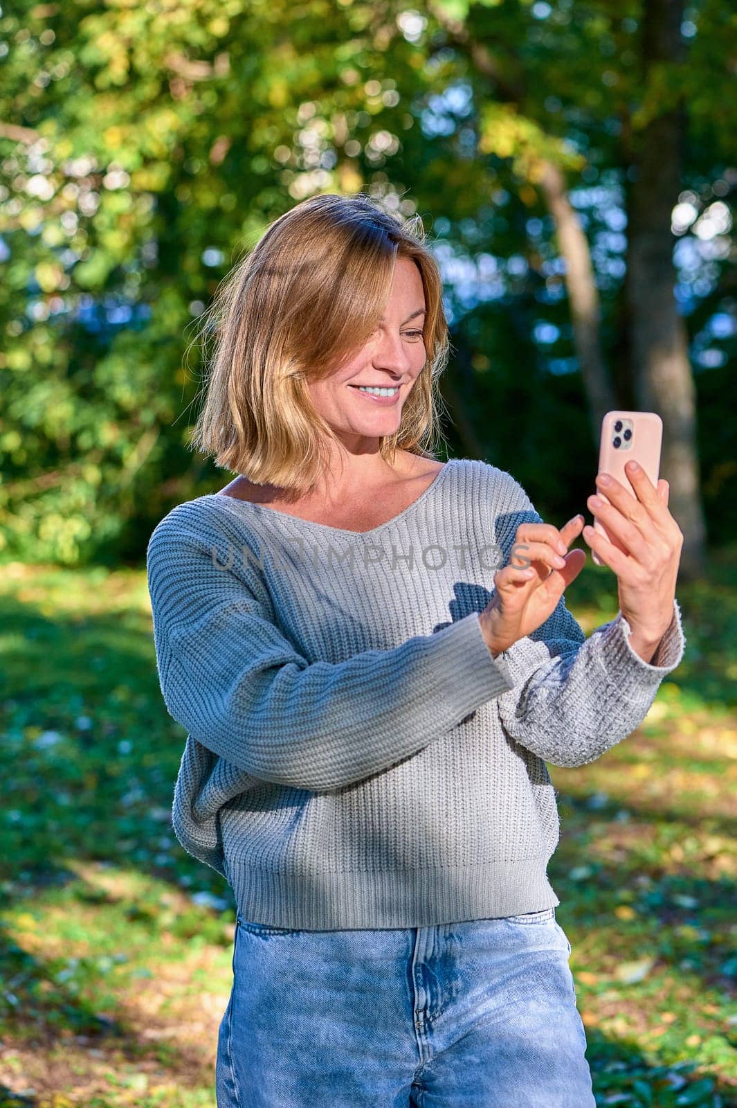 A woman in a park in the summer speaks during a video call on the phone. High quality photo