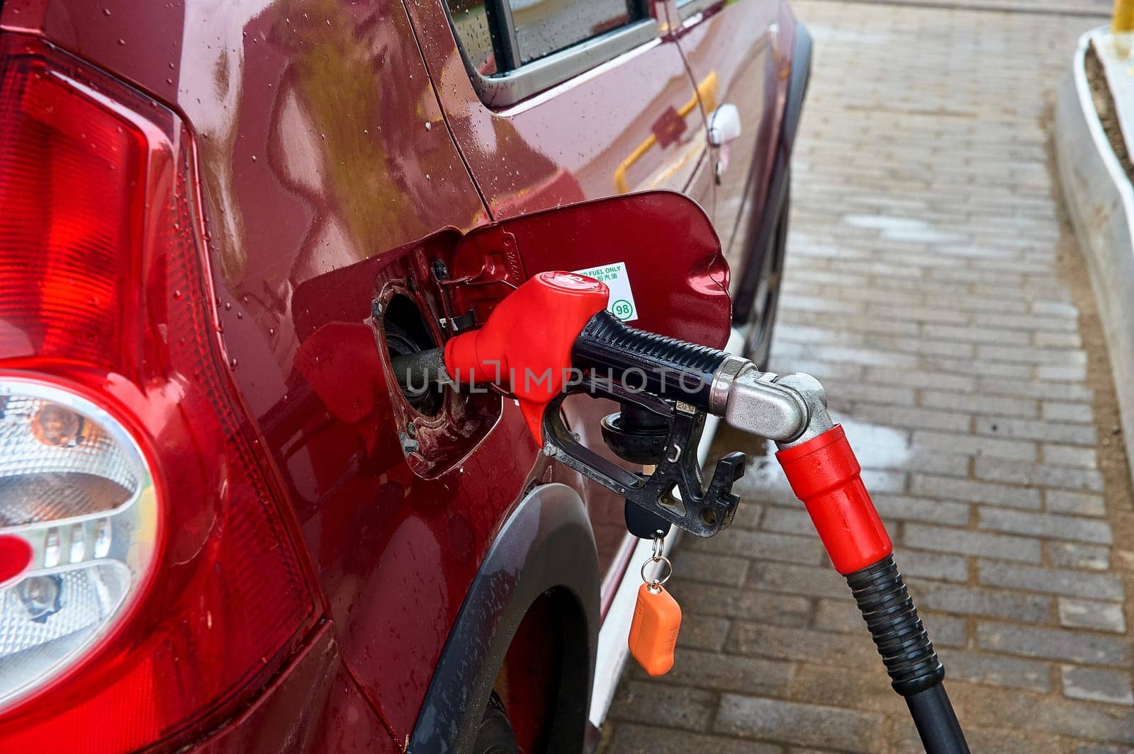 the red pistol is inserted into the gas tank of a red passenger car for refueling with gasoline. High quality photo