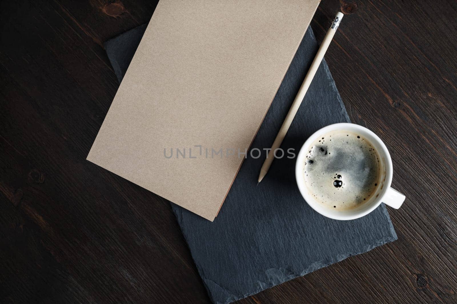 Blank kraft notepad, pencil and coffee cup on stone board. Flat lay.