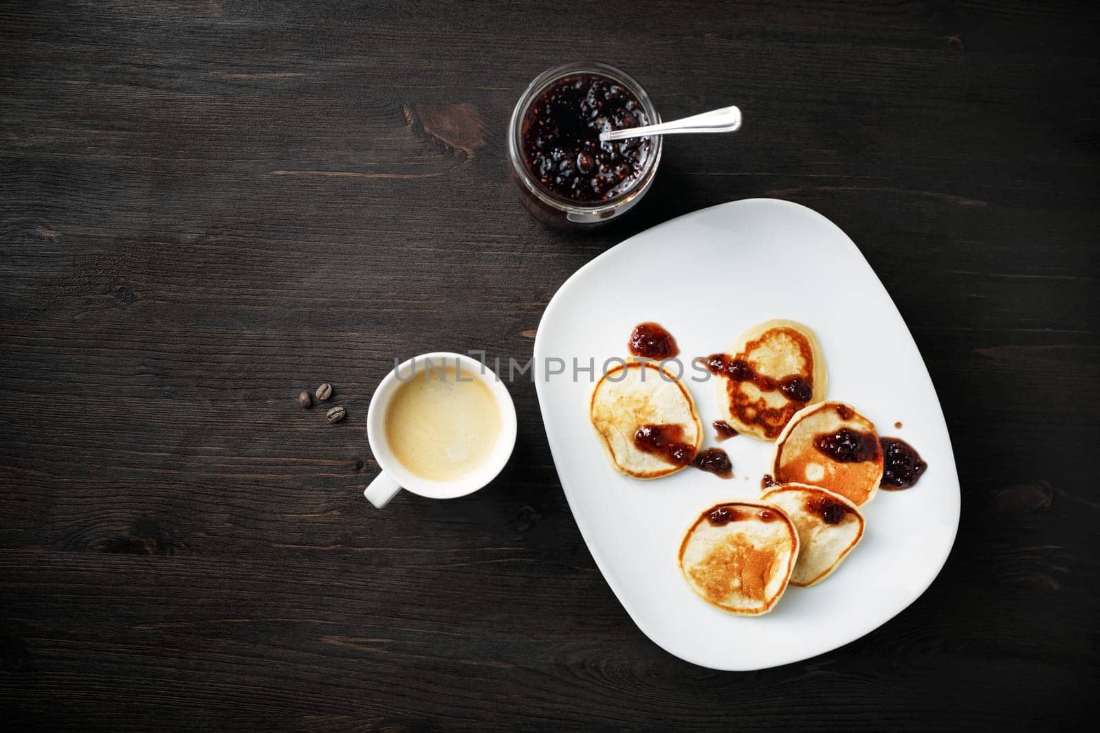 Pancakes with jam and coffee cup on wooden table background. Flat lay.