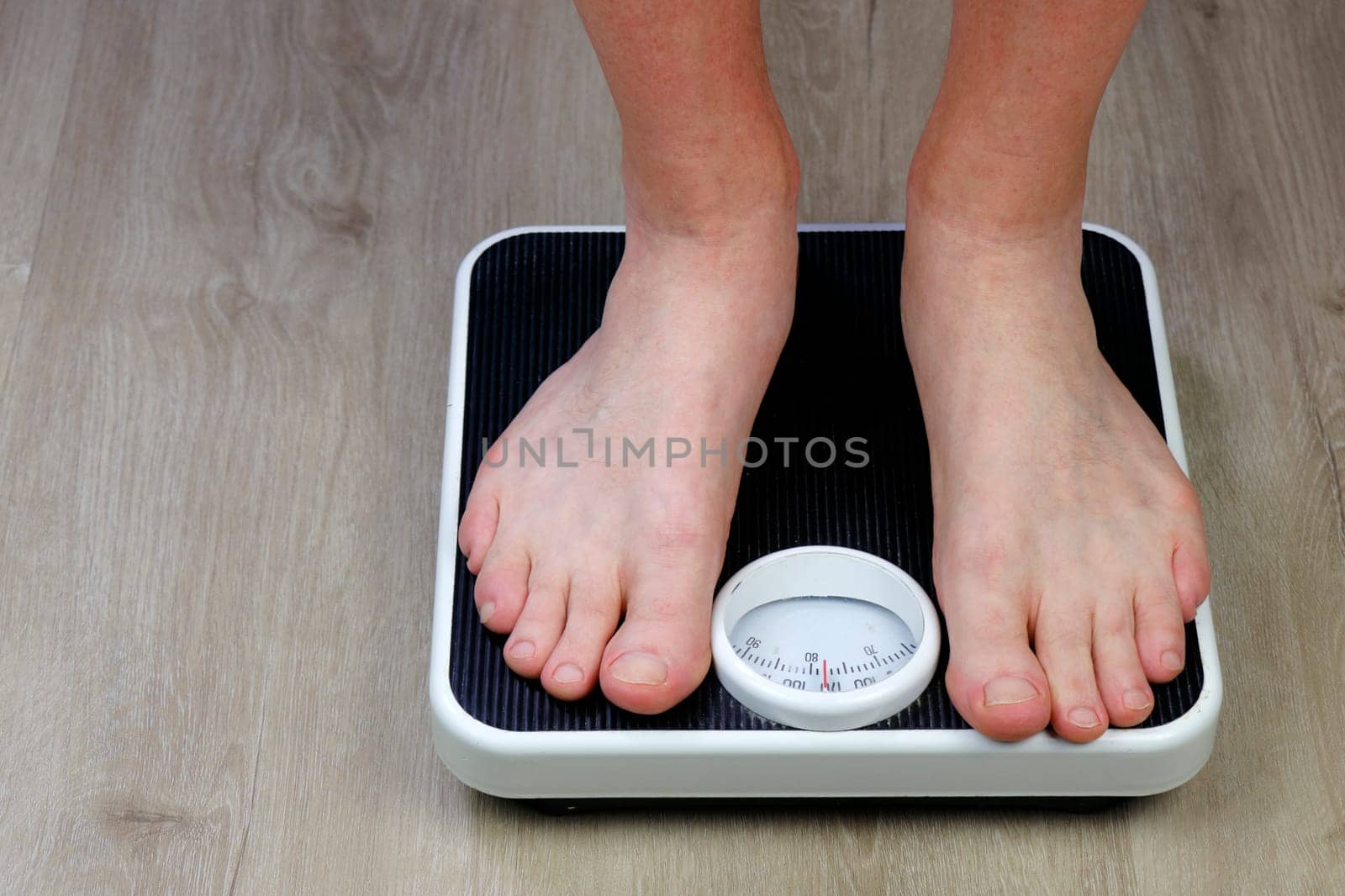 Adult man with bare feet standing on an old black and white weight scale on a vinyl floor. Bare feet of a caucasian man pointed towards the viewer standing on an old black and white weight scale.