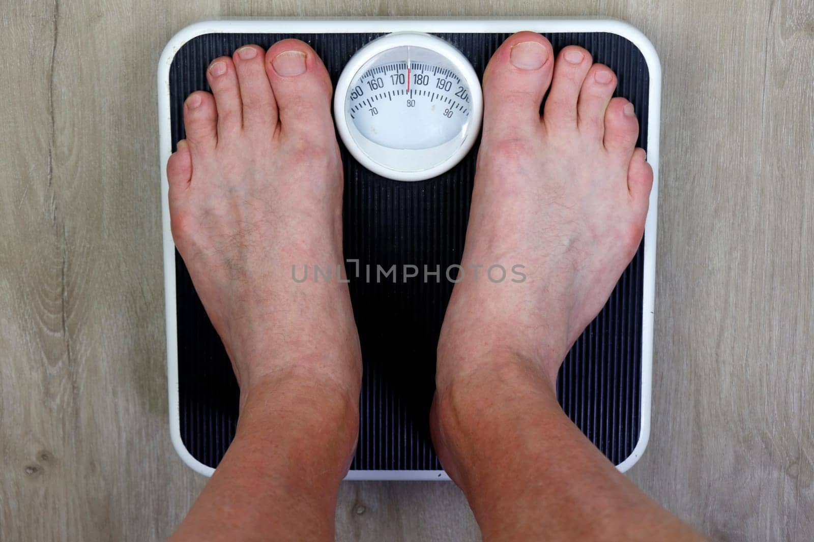 Old weight scale stood on my adult male seeing point of view of scale standing on. Adult white male weighing his self on an old worn black and white weight scale on a wood grain design vinyl floor.
