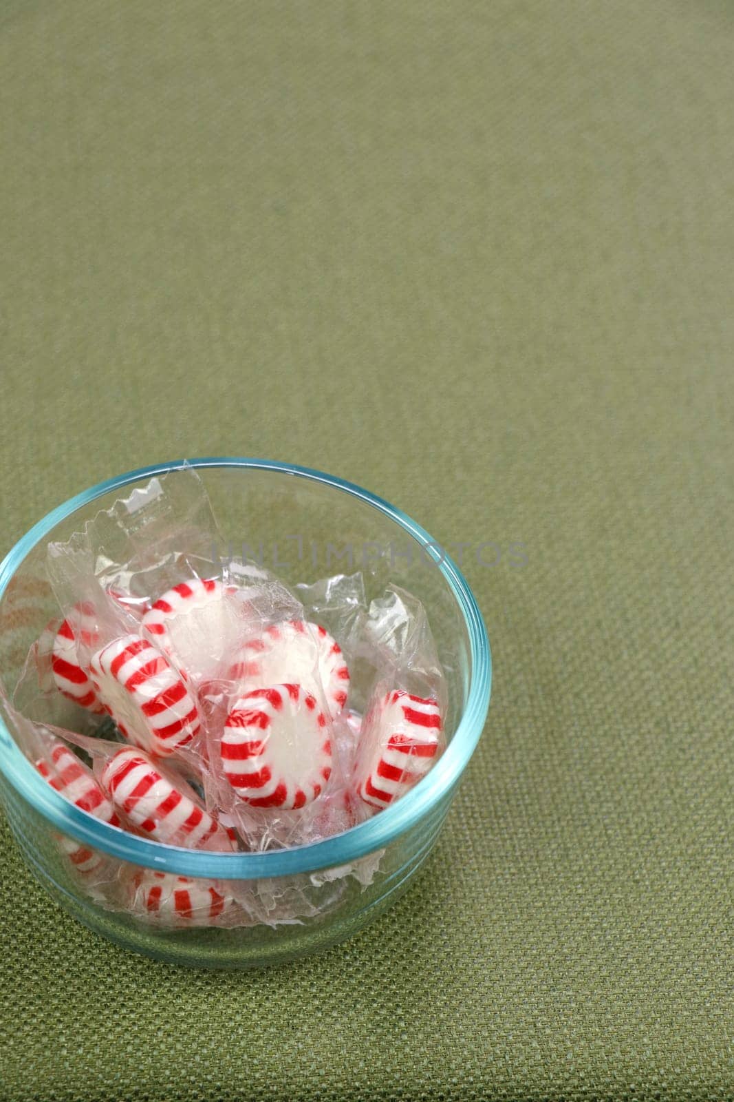 Individually wrapped with clear plastic white and red peppermint hard candy discs in a glass bowl on a green tablecloth. White and red peppermint hard candy in a clear bowl on a green tablecloth.