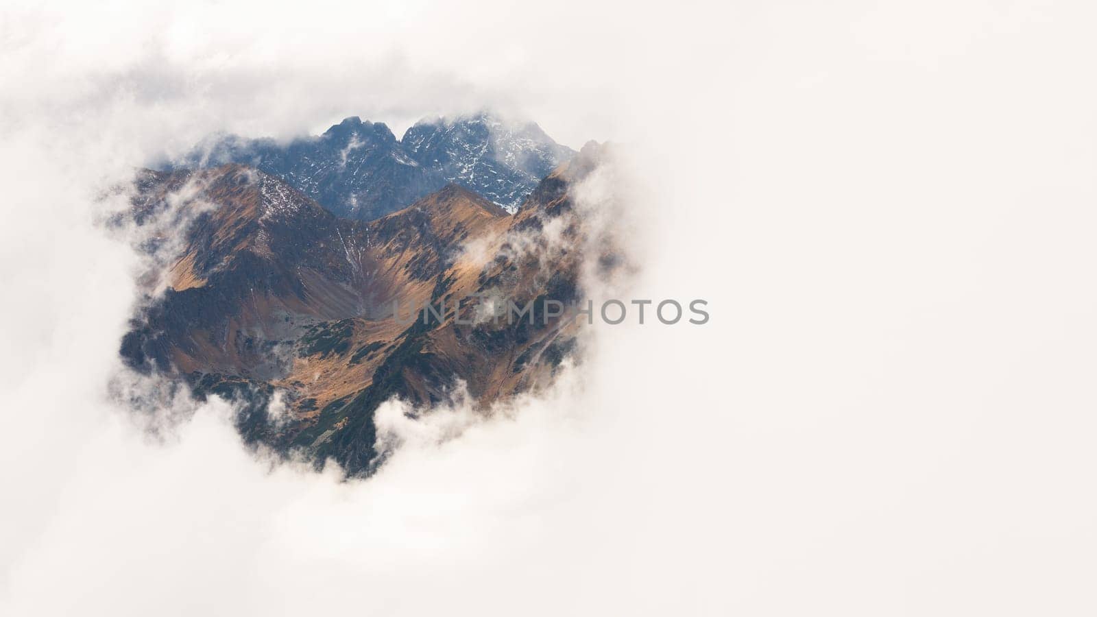 Mysterious mountains covered by a thick fog in nature. A see through window to a slopes and valleys of High Tatras national park, Slovakia. Horizontal landscape with rocky hills behind a mist.