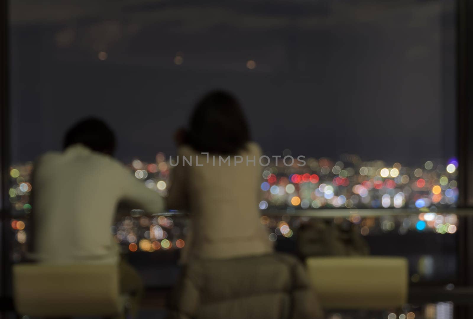 Blur couple sitting on skyscraper observatory overlooking the city aerial view at night
