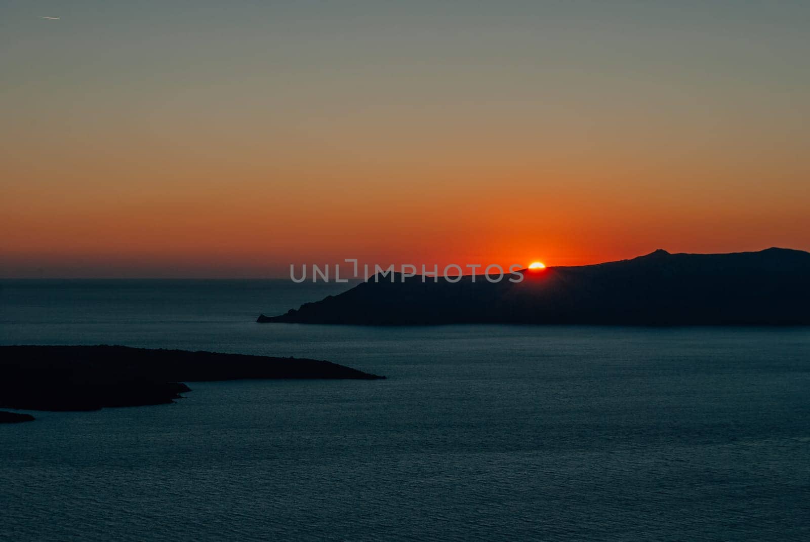 The sun at sunset almost disappeared behind the island, Santorini, Greece.