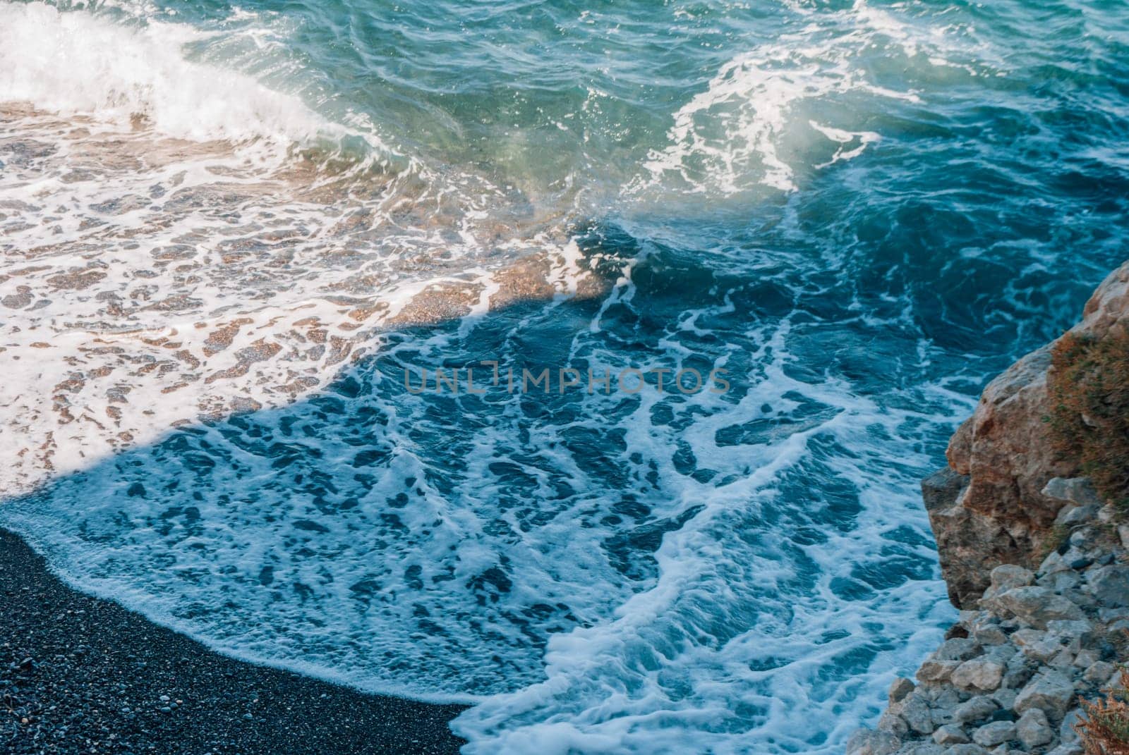 Waves, rock and black sand on Kamari Beach, Santorini, Greece.