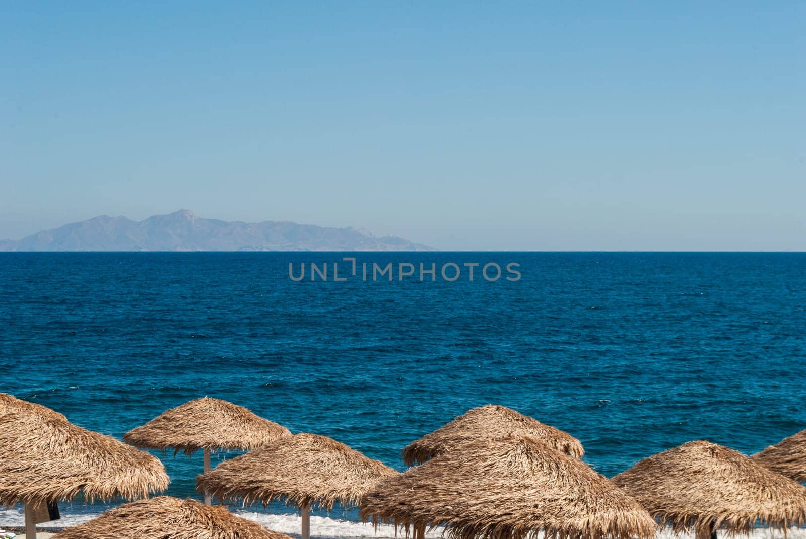 Straw beach umbrellas against the blue sea and sky.