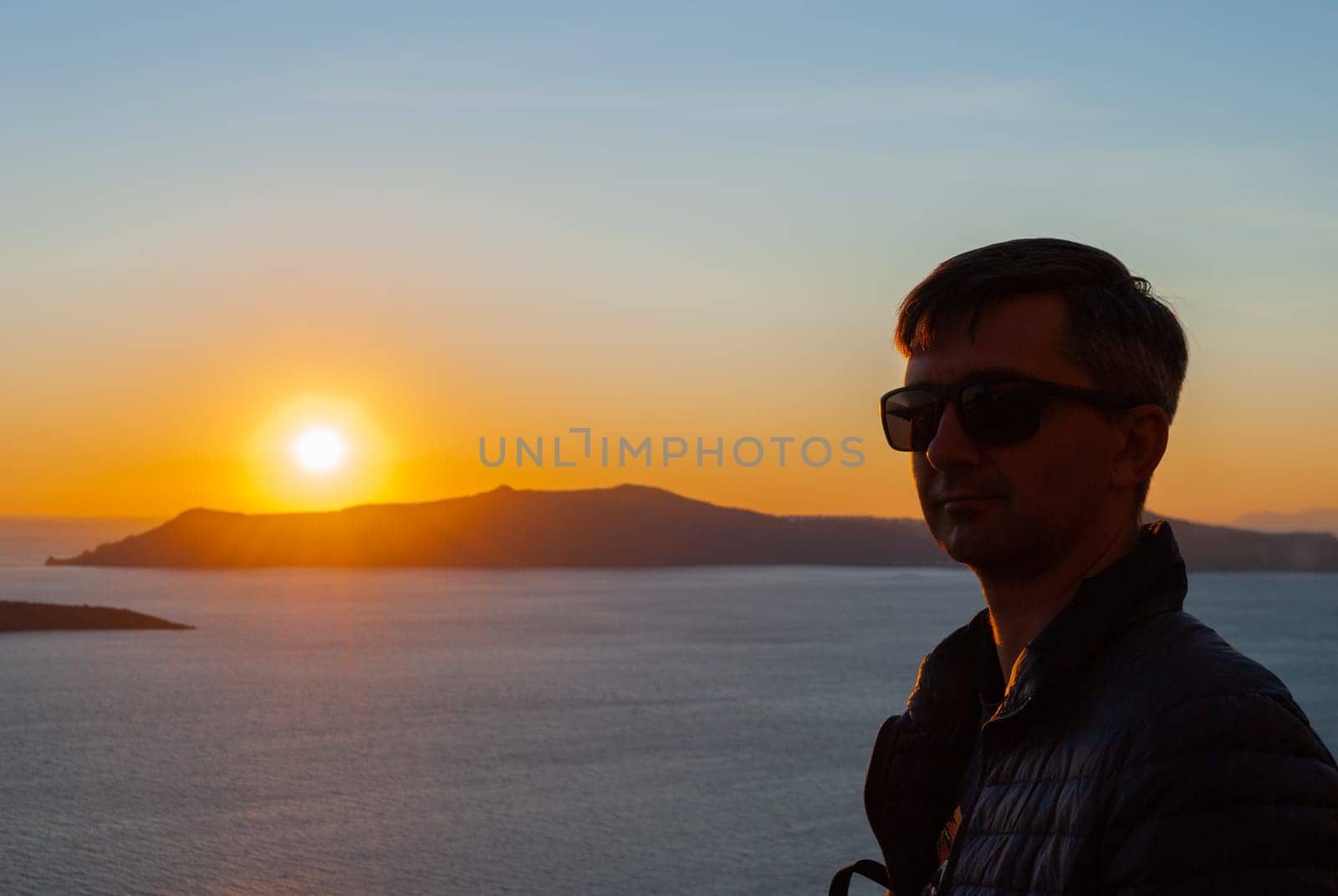 Silhouette of a man's head and shoulders in the background of a sunset in Santorini, Greece.