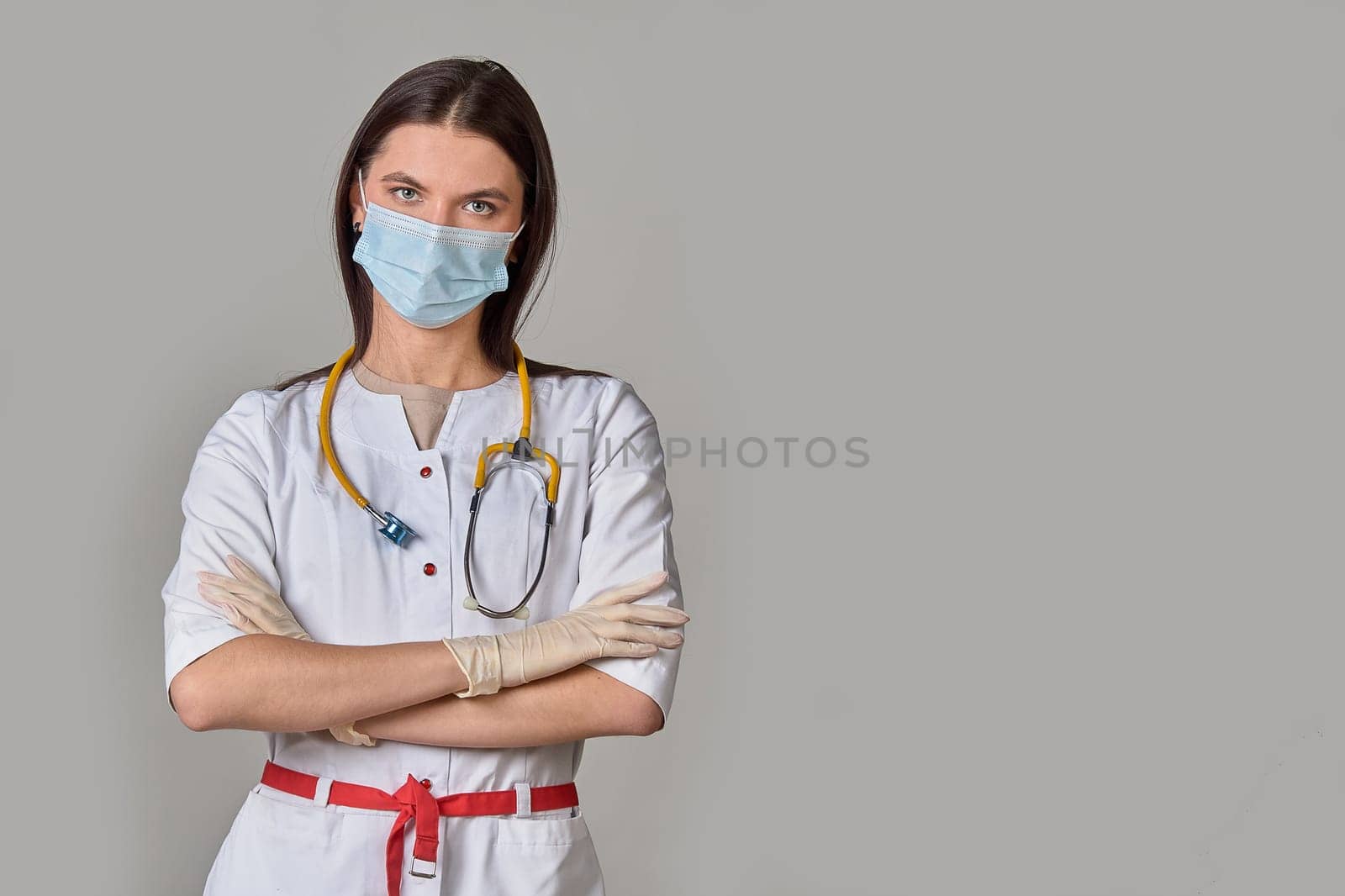 A young female doctor in a white coat with a stethoscope and a medical mask on a gray isolated background. copy space. High quality photo