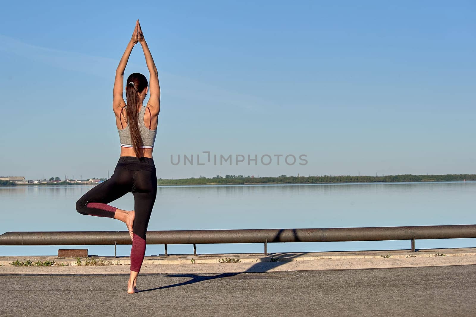 A young woman does a warm-up on the pier in the early morning, against the background of the river. High quality photo