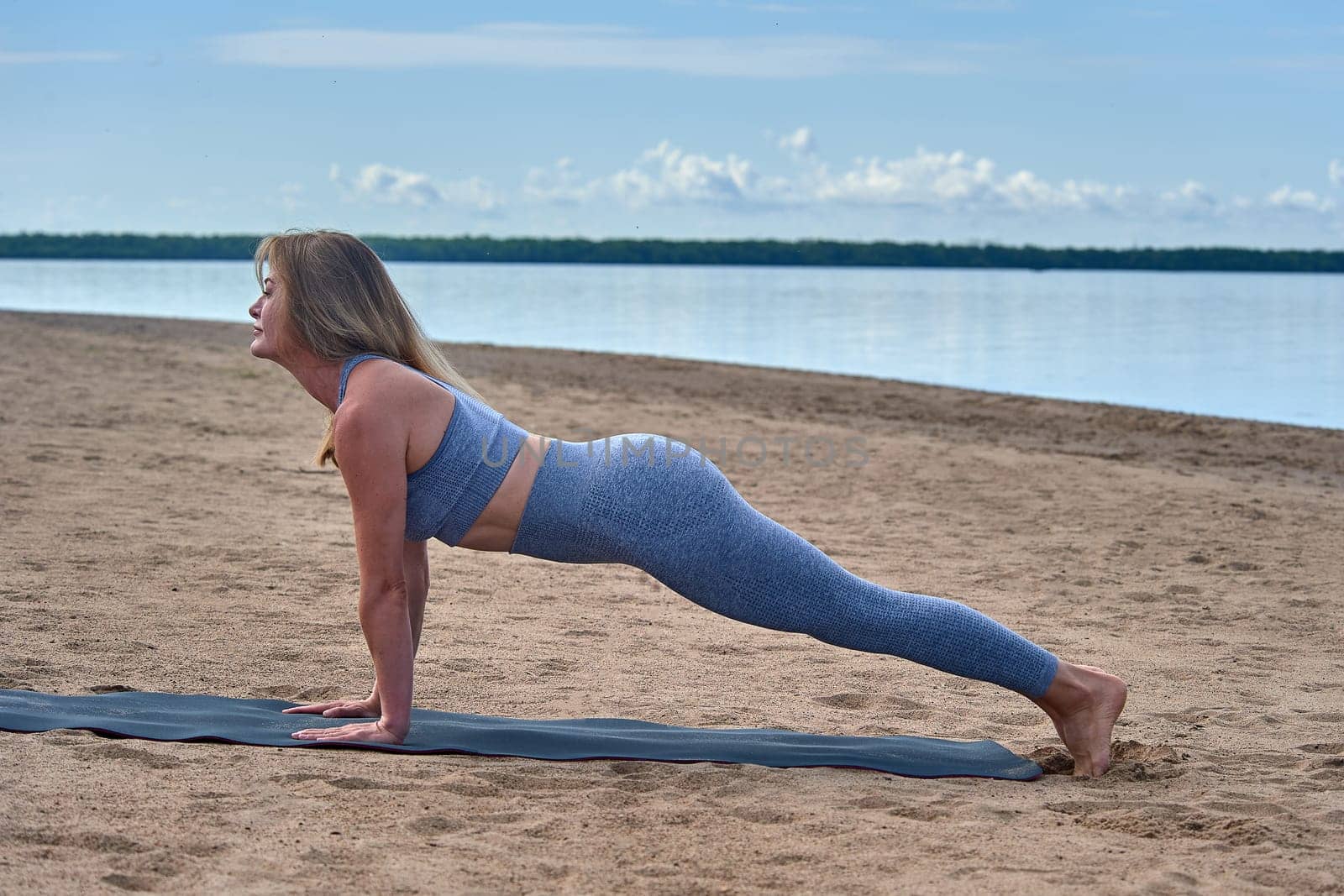 A woman does yoga on a sandy beach against the background of a river. High quality photo