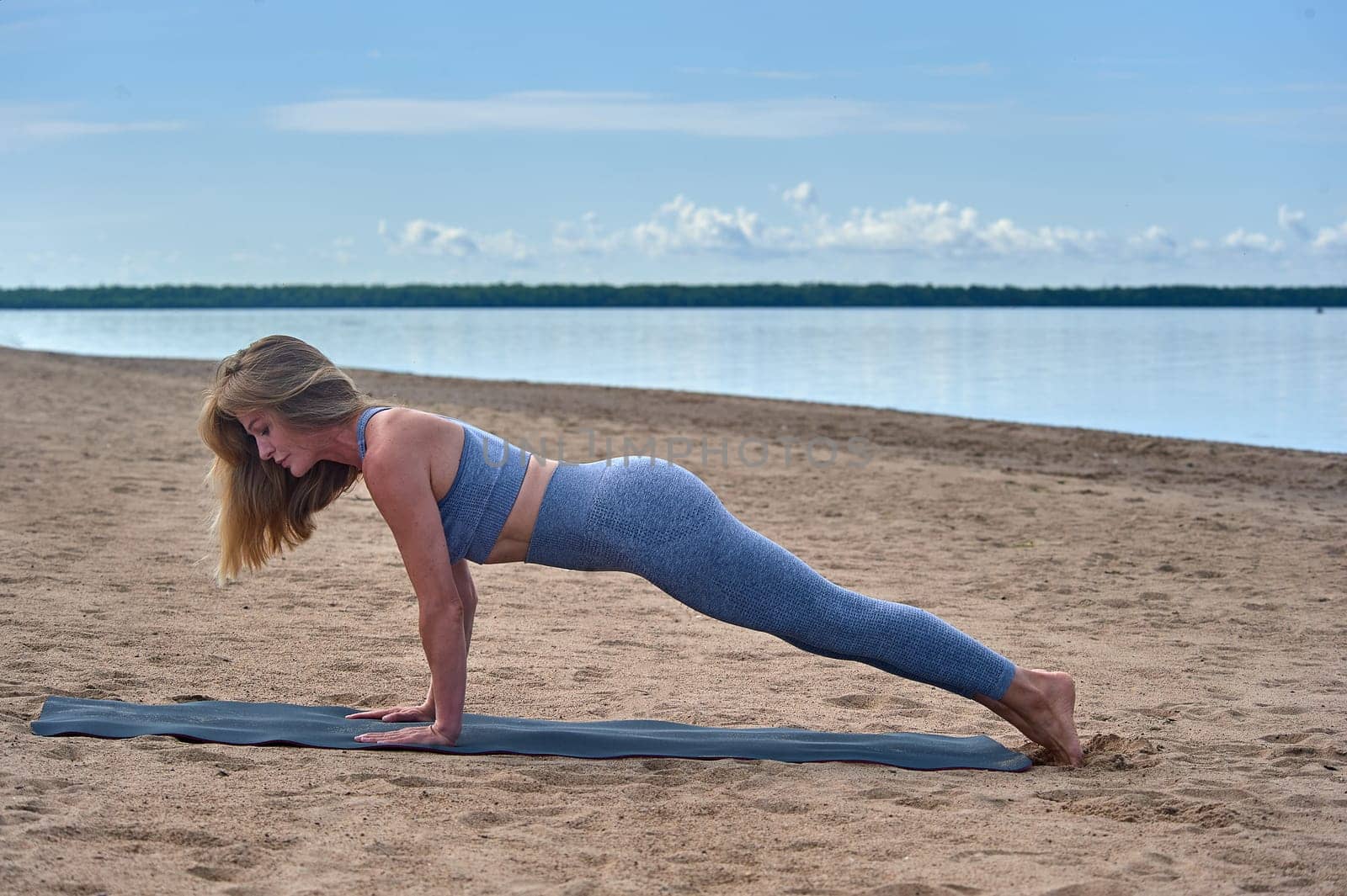 A woman does yoga on a sandy beach against the background of a river. High quality photo