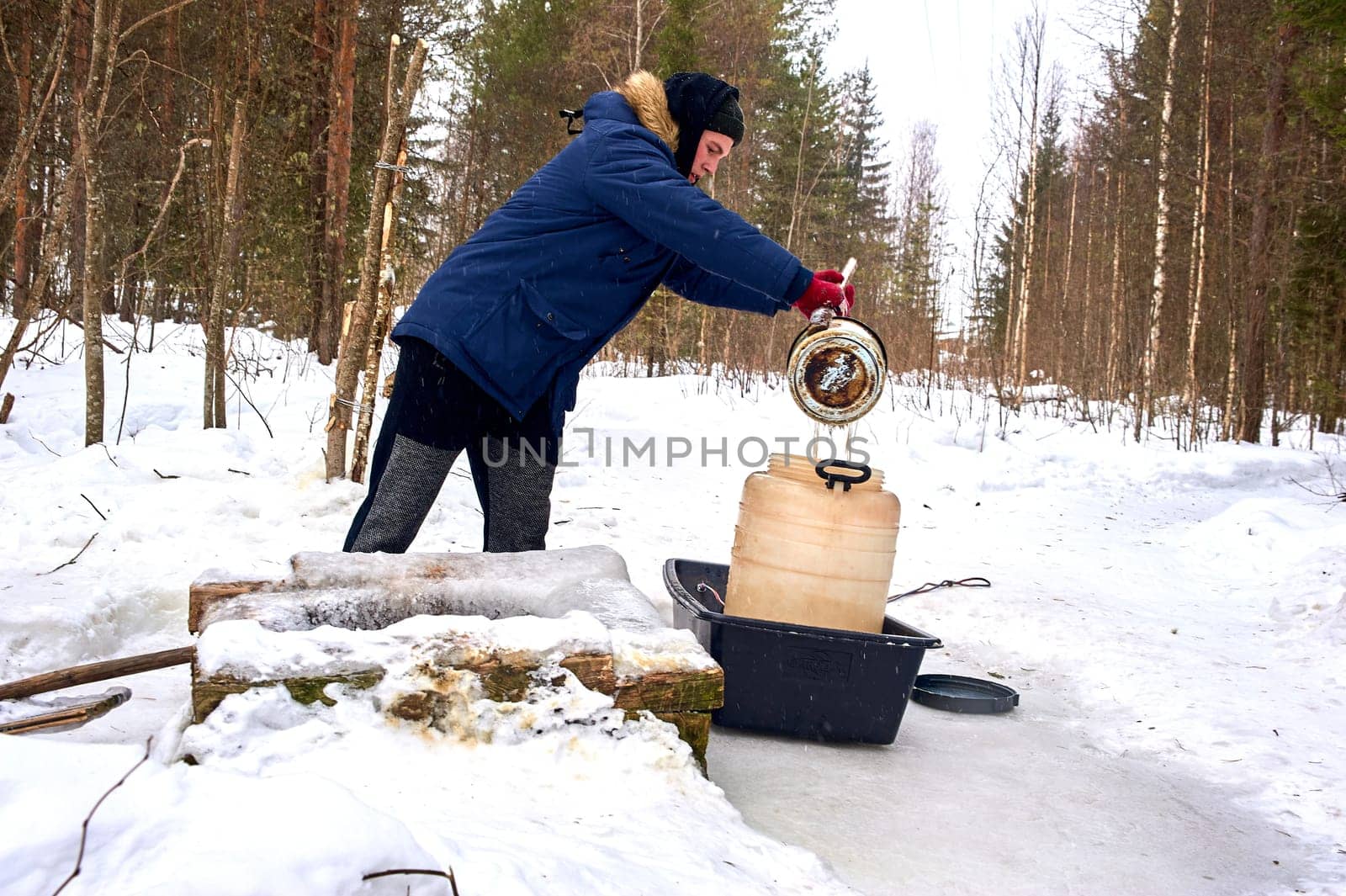 A man draws water from a spring in a plastic barrel in winter. High quality photo