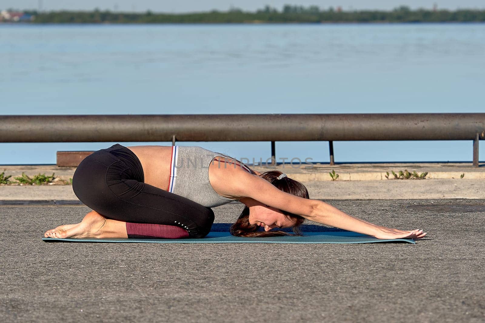 A young woman does a warm-up on the pier in the early morning, against the background of the river. High quality photo