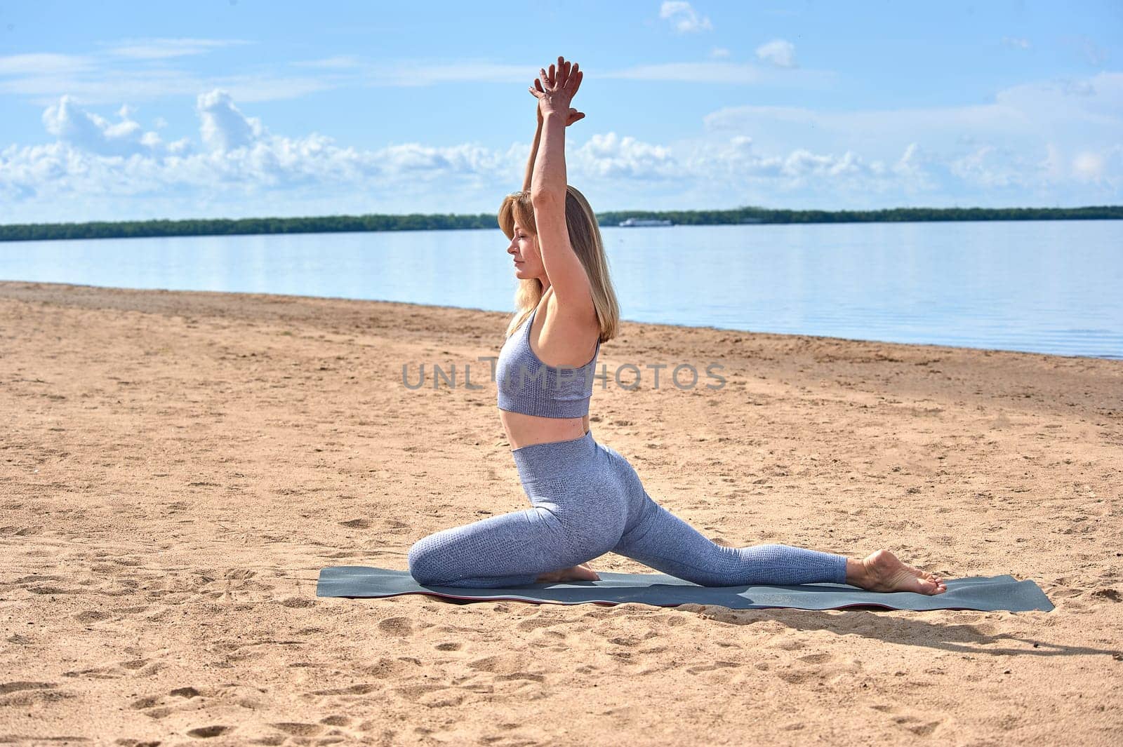 A woman does yoga on a sandy beach against the background of a river. High quality photo