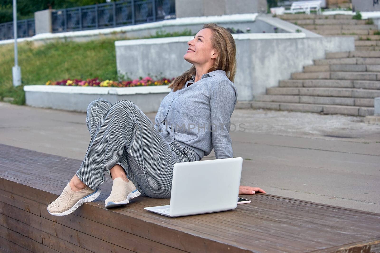 A woman with a laptop sits on a wooden platform, works online. High quality photo