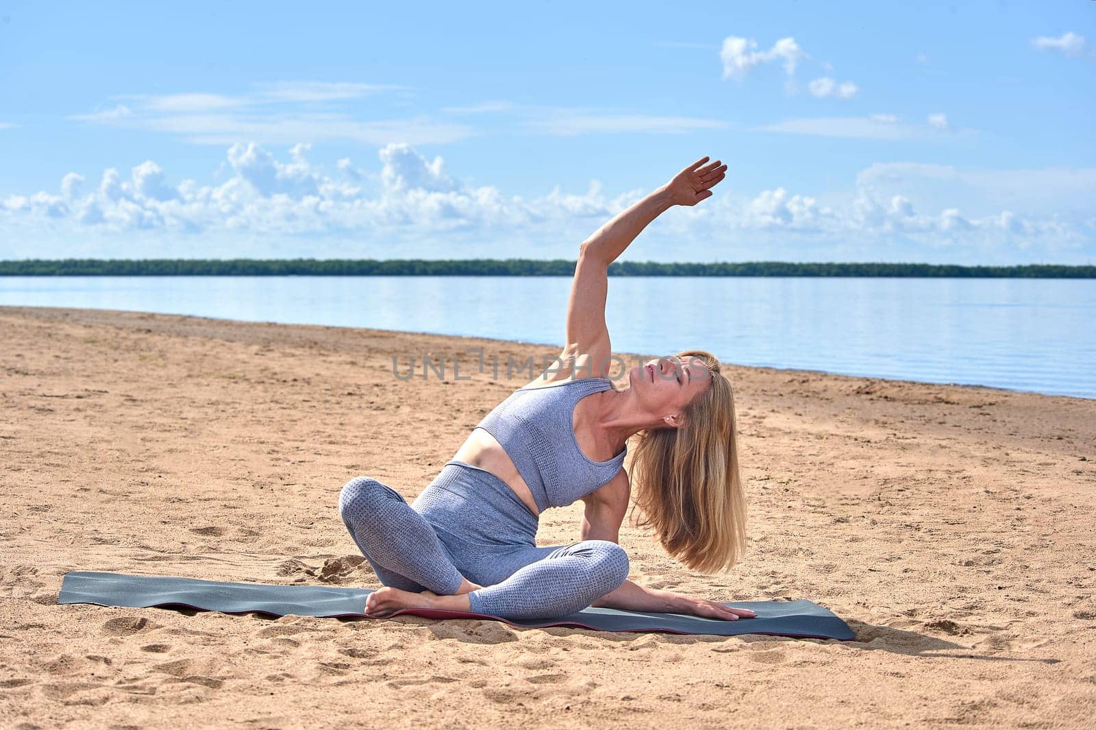 A woman does yoga on a sandy beach against the background of a river. High quality photo